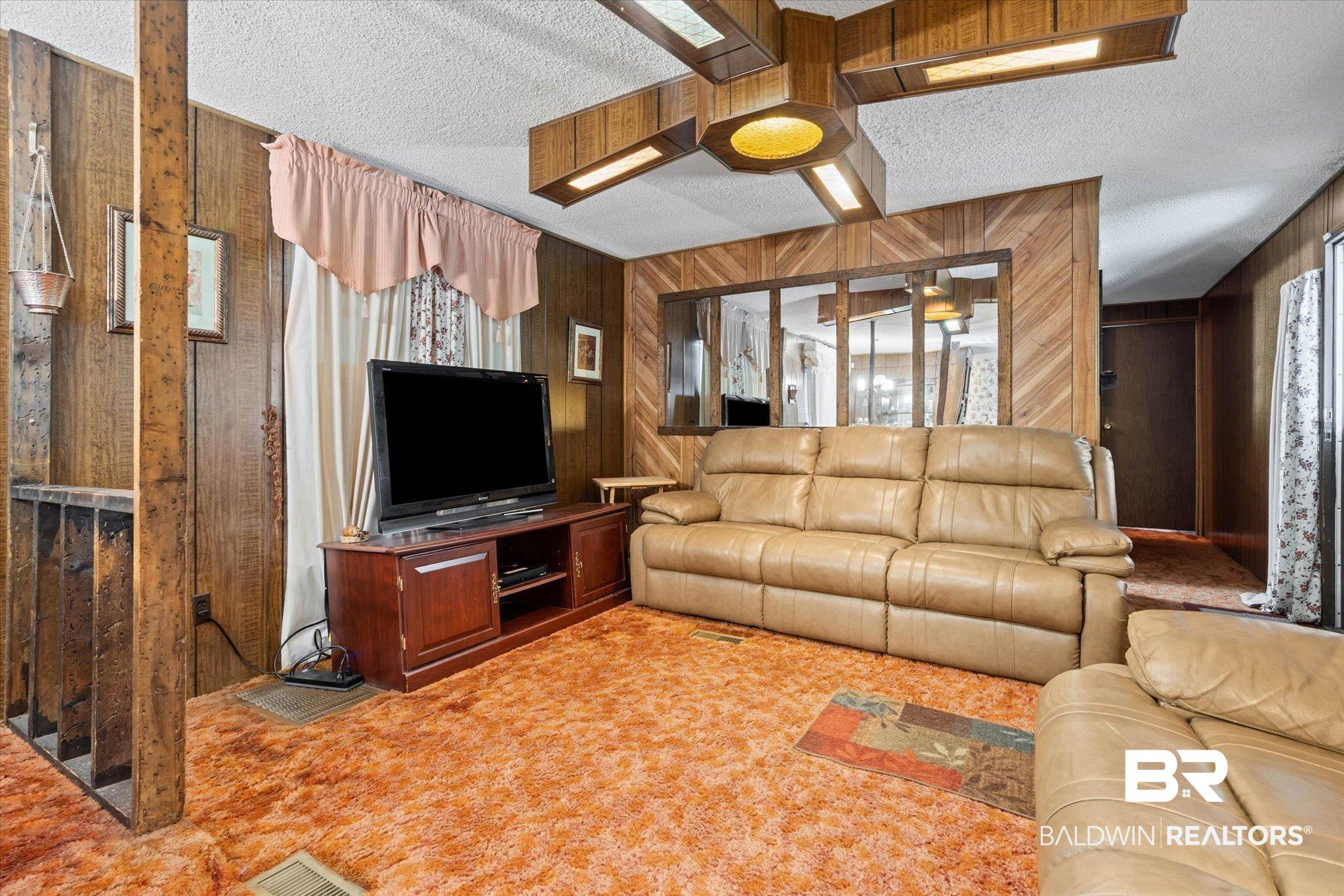 Image 4: Living area with wood-finish paneling, textured ceiling, and orange carpet flooring