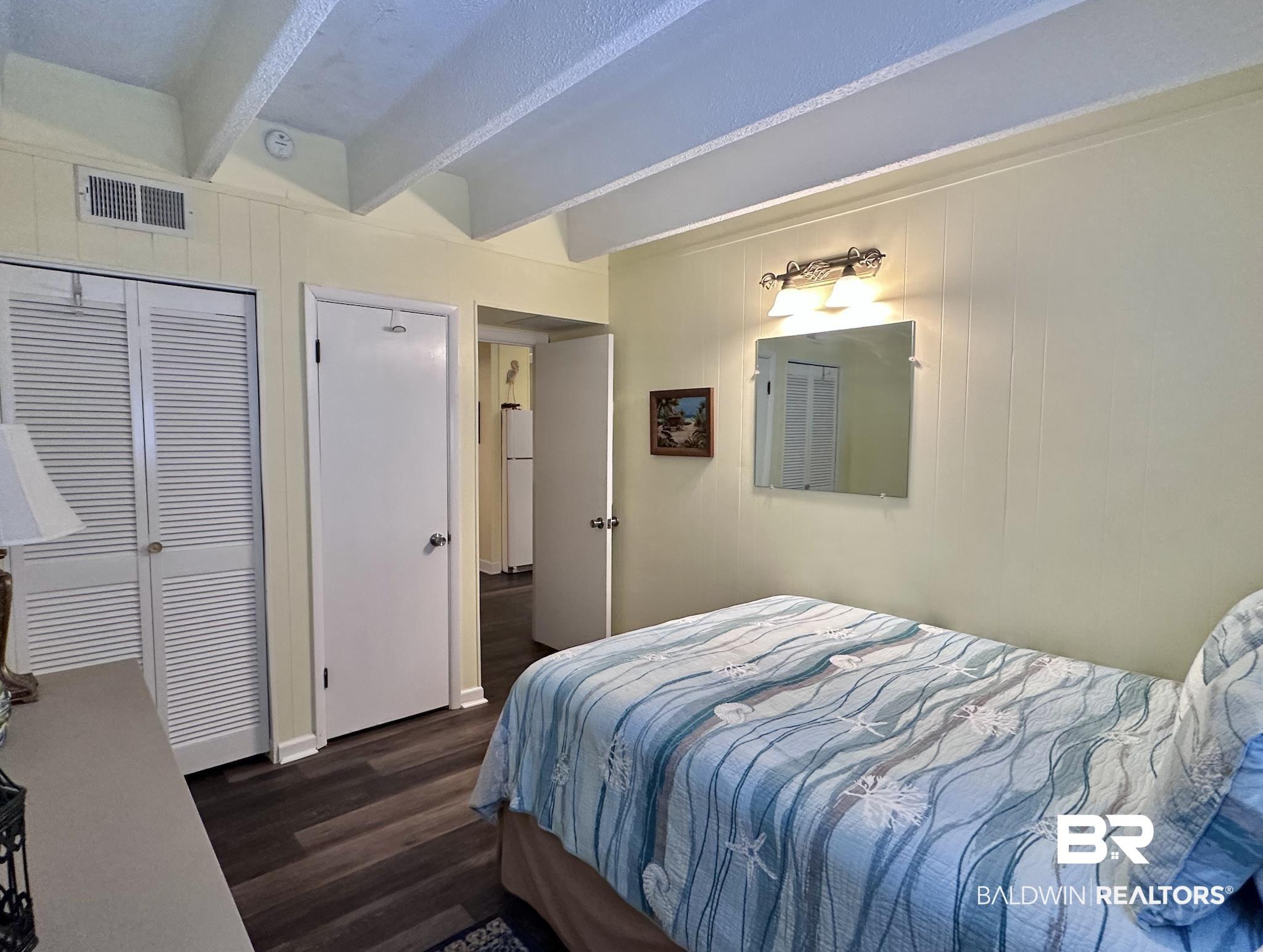 Image 3: Bedroom with beam ceiling, dark wood-style flooring, a closet, wooden walls, and freestanding refrigerator
