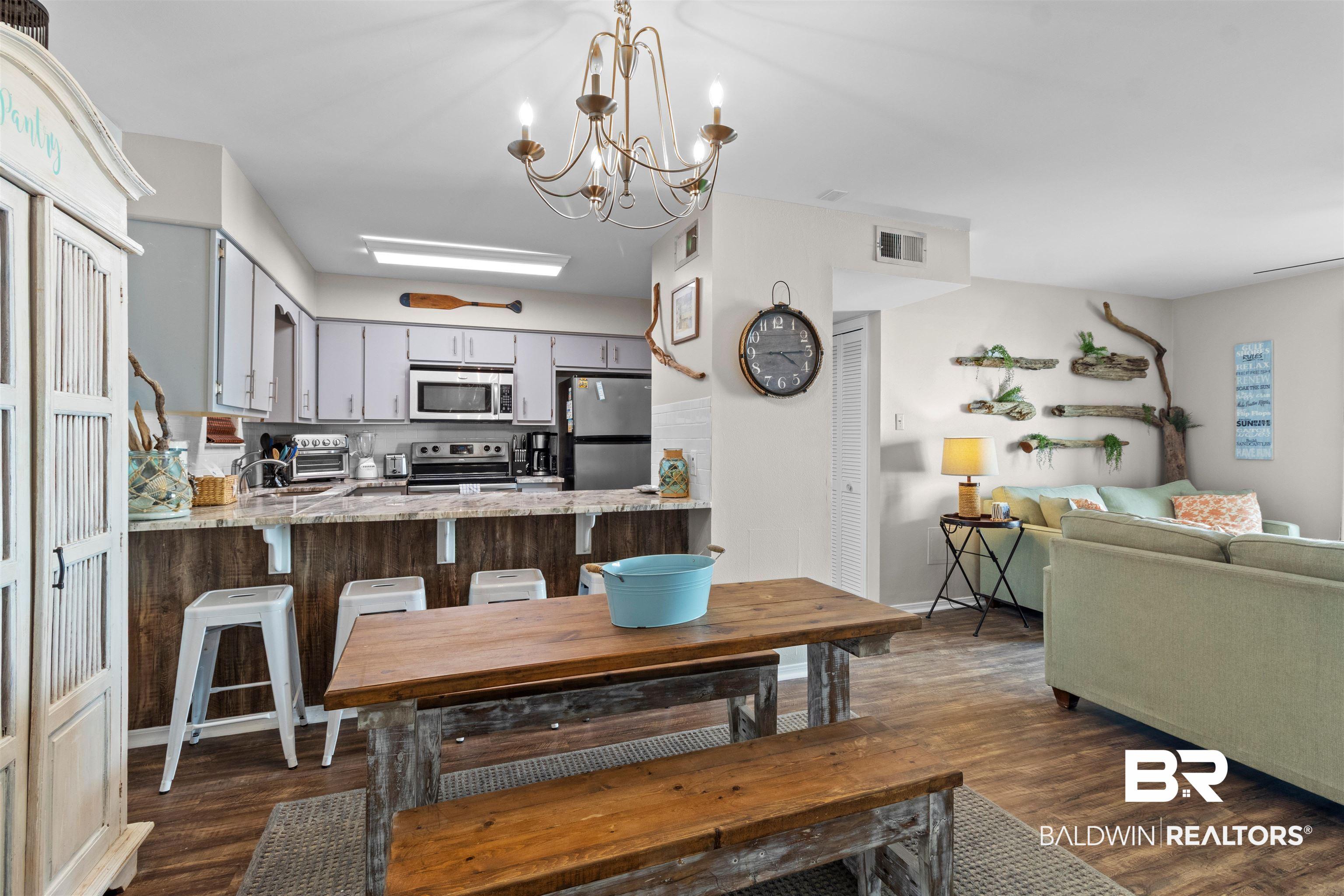 Image 4: Open-concept kitchen and dining area featuring wood-finish flooring, a breakfast bar with seating, light-toned cabinetry, and stainless steel appliances