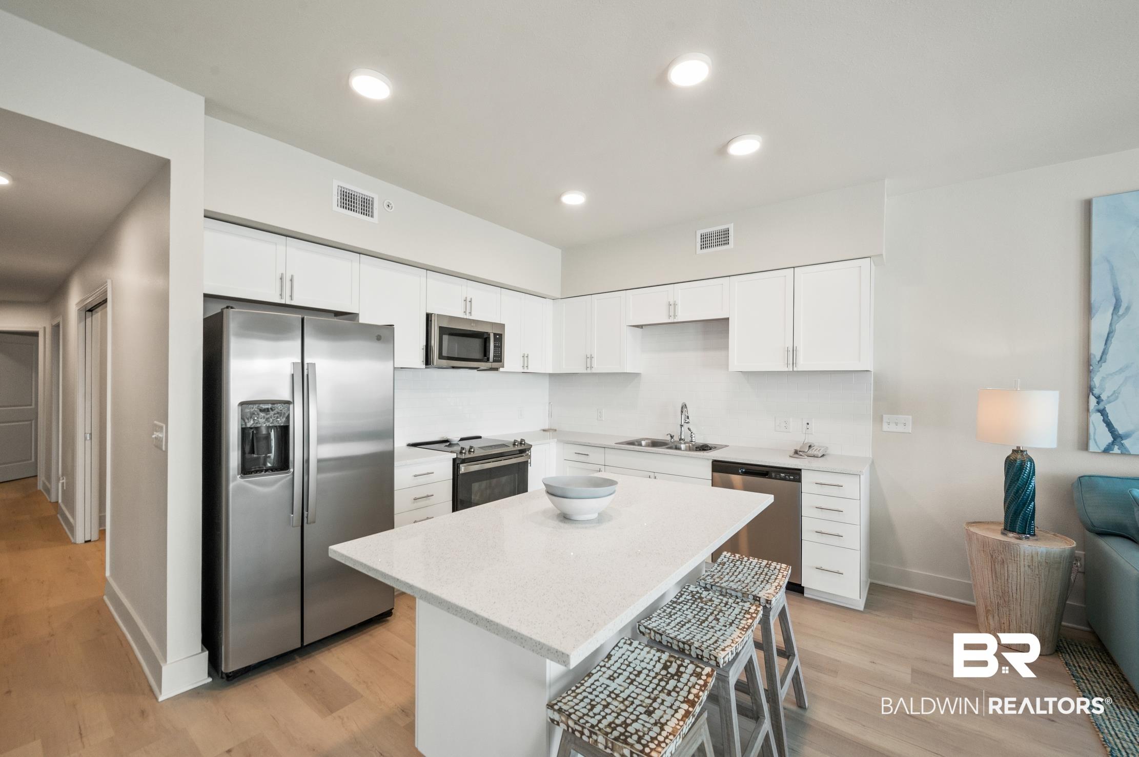 Image 4: Kitchen featuring white shaker cabinetry, stainless steel appliances, light quartz countertops, a kitchen island with seating, and wood-finish flooring