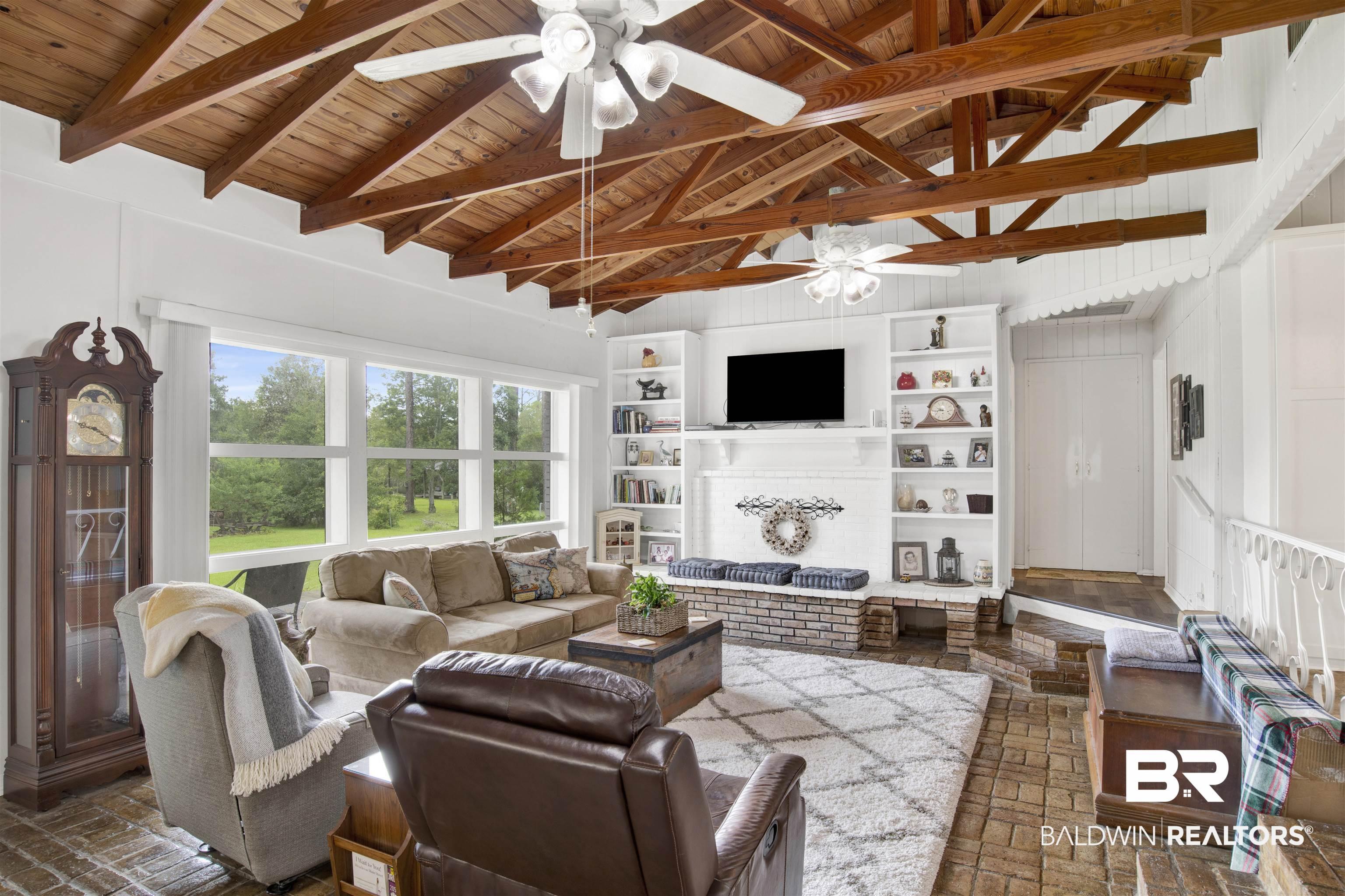 Image 4: Living room featuring a ceiling fan, a brick fireplace, brick flooring, a wood ceiling with exposed beams, and built in shelves