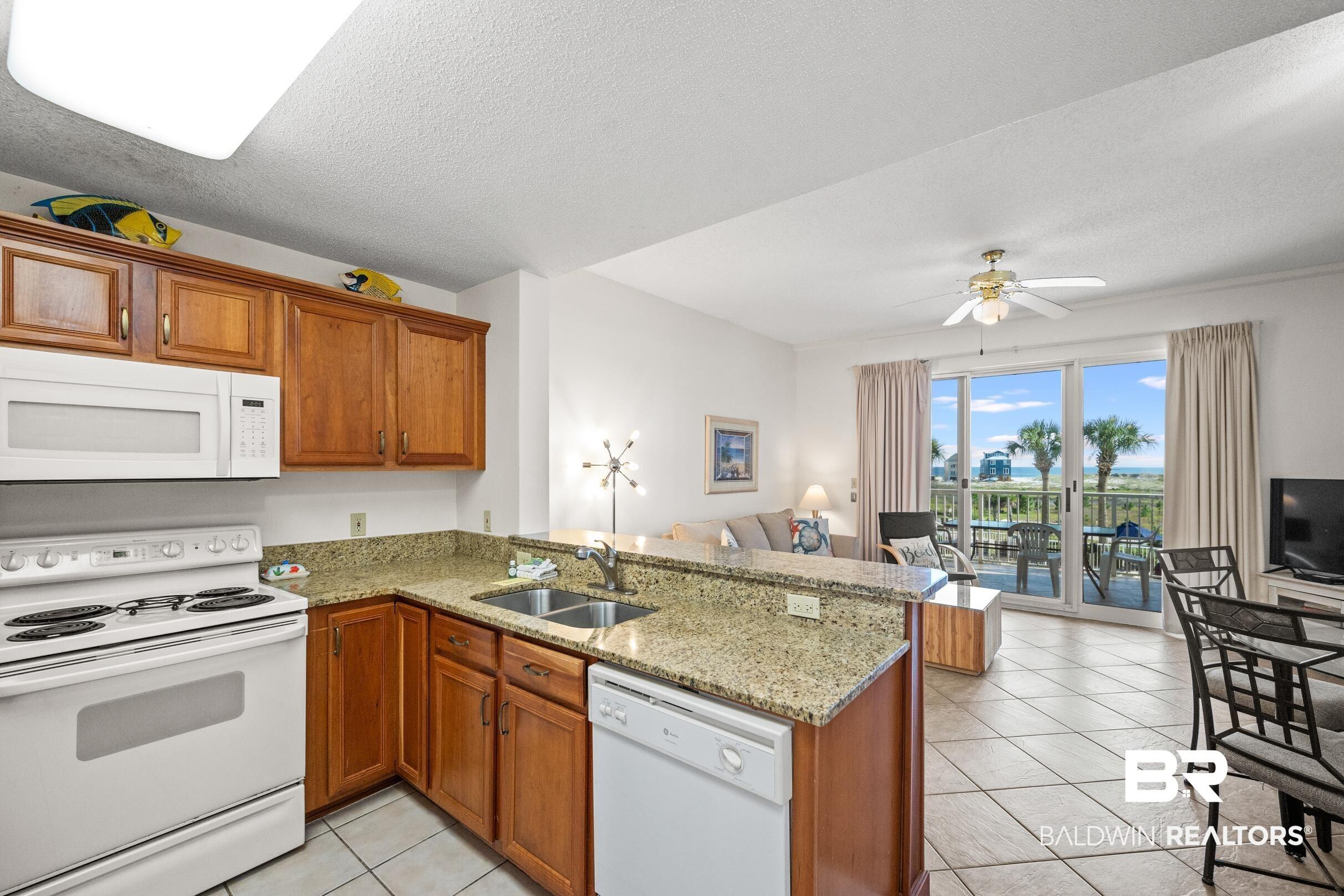 Image 2: Kitchen with brown cabinets, open floor plan, a sink, white appliances, and a peninsula
