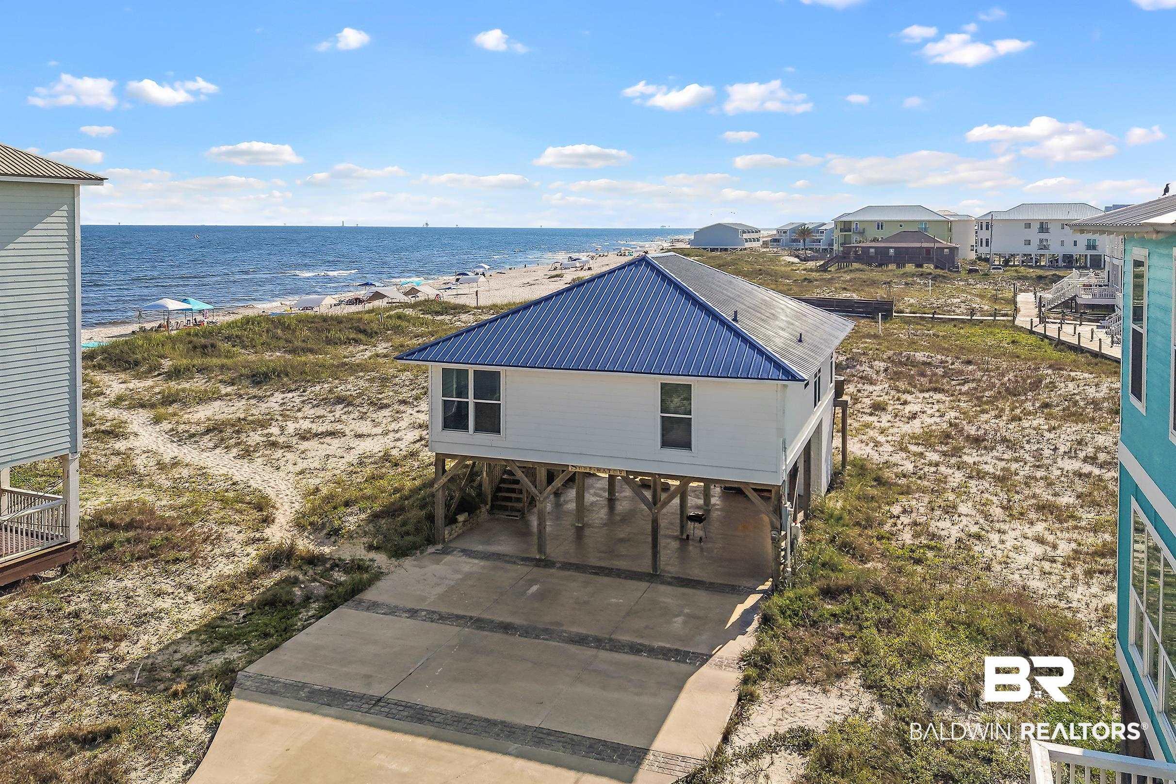 Image 2: Stilted coastal home featuring a blue metal roof and white siding