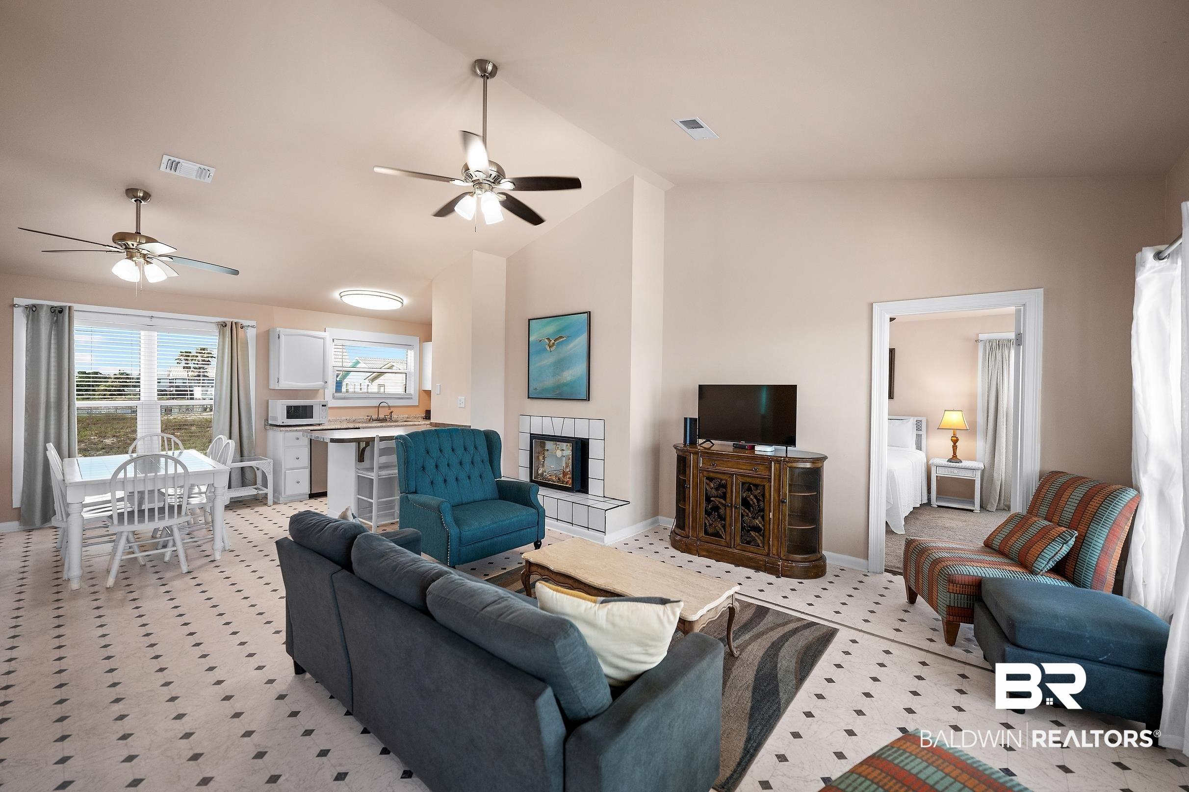 Image 3: Open-concept living space featuring a fireplace with white tile surround, vaulted ceiling, and patterned tile flooring
