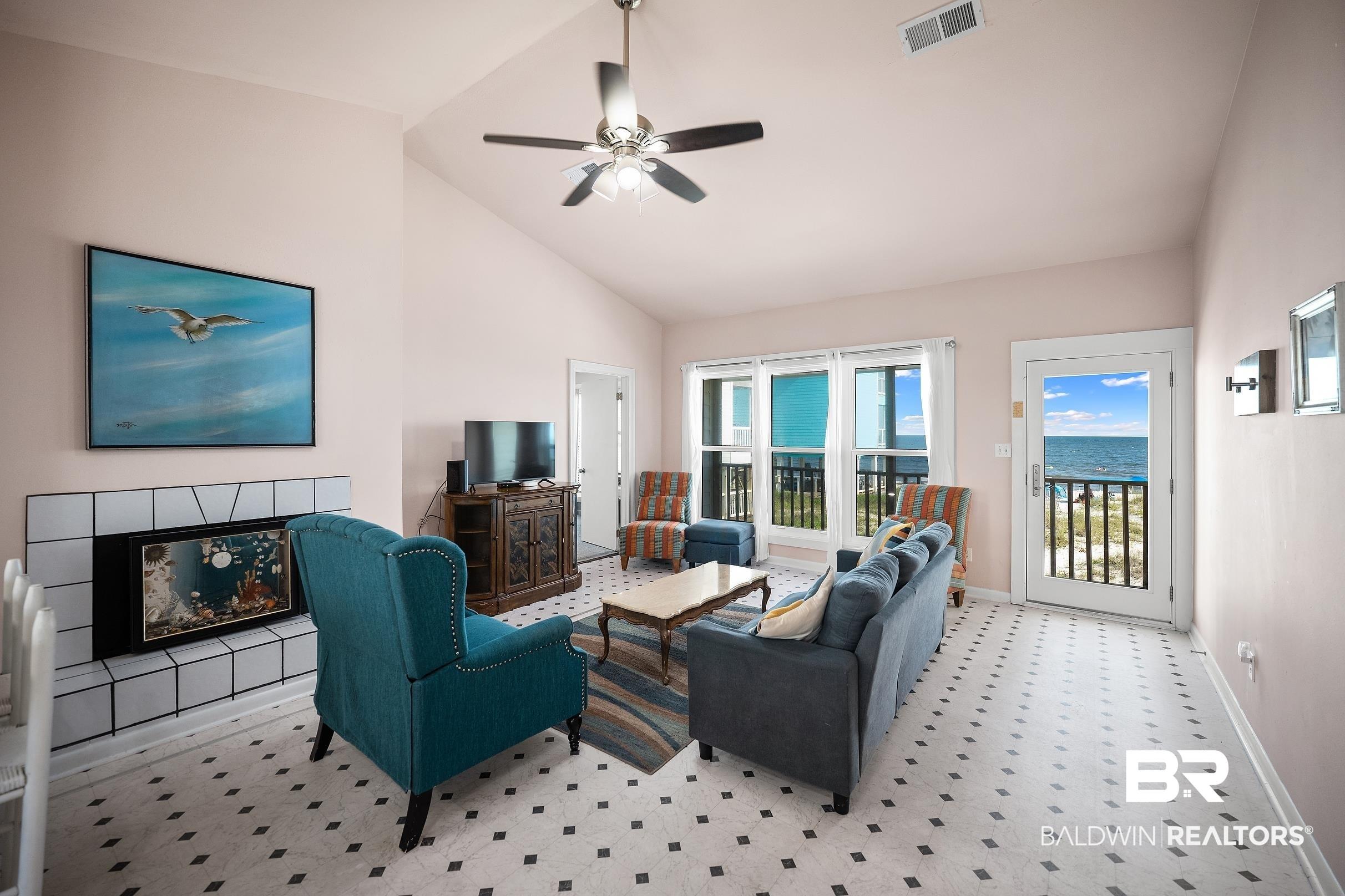 Image 4: Spacious living area featuring a vaulted ceiling with a ceiling fan, a tiled fireplace, and diamond-patterned tile flooring