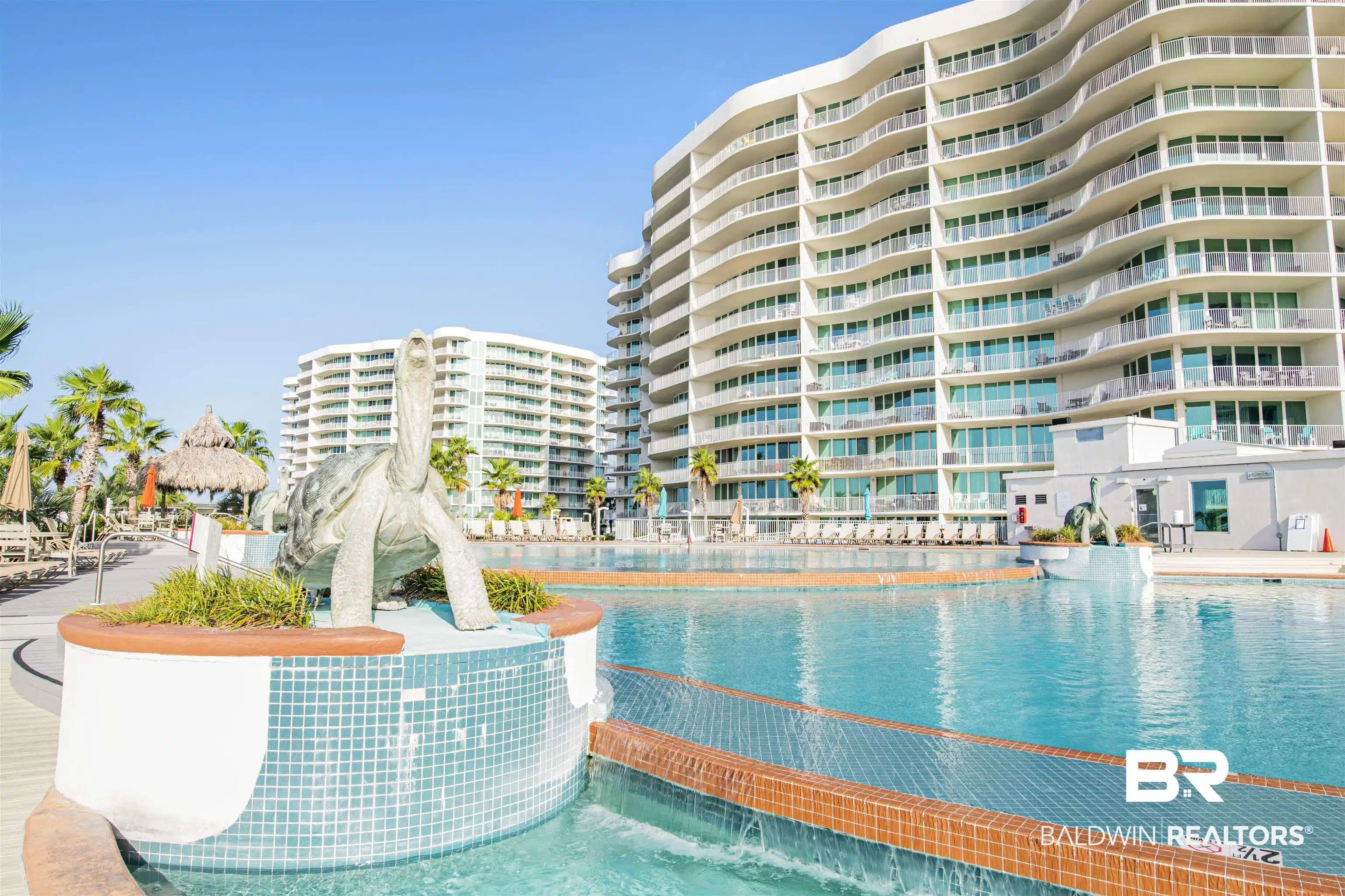 Image 1: Expansive outdoor pool area featuring a turtle sculpture, surrounding lounge seating, and lush palm trees