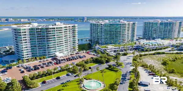 Image 2: Expansive waterfront property featuring multiple high-rise buildings with balconies, extensive parking areas, a landscaped entrance with a fountain, and direct water access