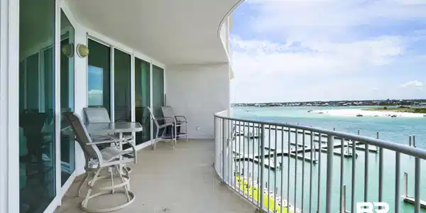Image 3: Curved balcony with concrete flooring and a white metal railing overlooking a marina with multiple boat slips