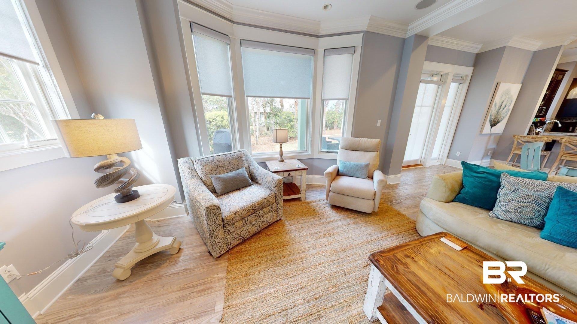 Image 2: Living area featuring light wood-finish flooring, a woven area rug, and a bay window with multiple paneled windows