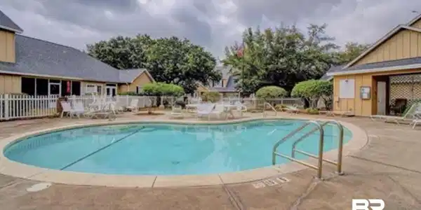 Image 4: Inviting swimming pool with concrete decking, surrounding buildings featuring siding, and mature landscaping