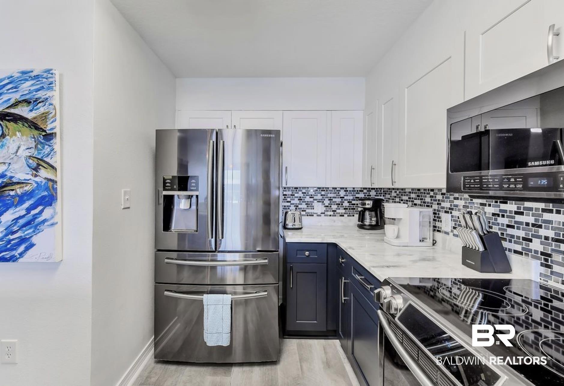 Image 4: Kitchen with white cabinetry, light wood-type flooring, backsplash, light stone counters, and appliances with stainless steel finishes