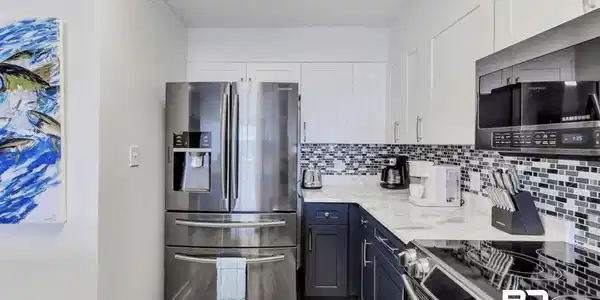 Image 4: Kitchen with white cabinetry, light wood-type flooring, backsplash, light stone counters, and appliances with stainless steel finishes