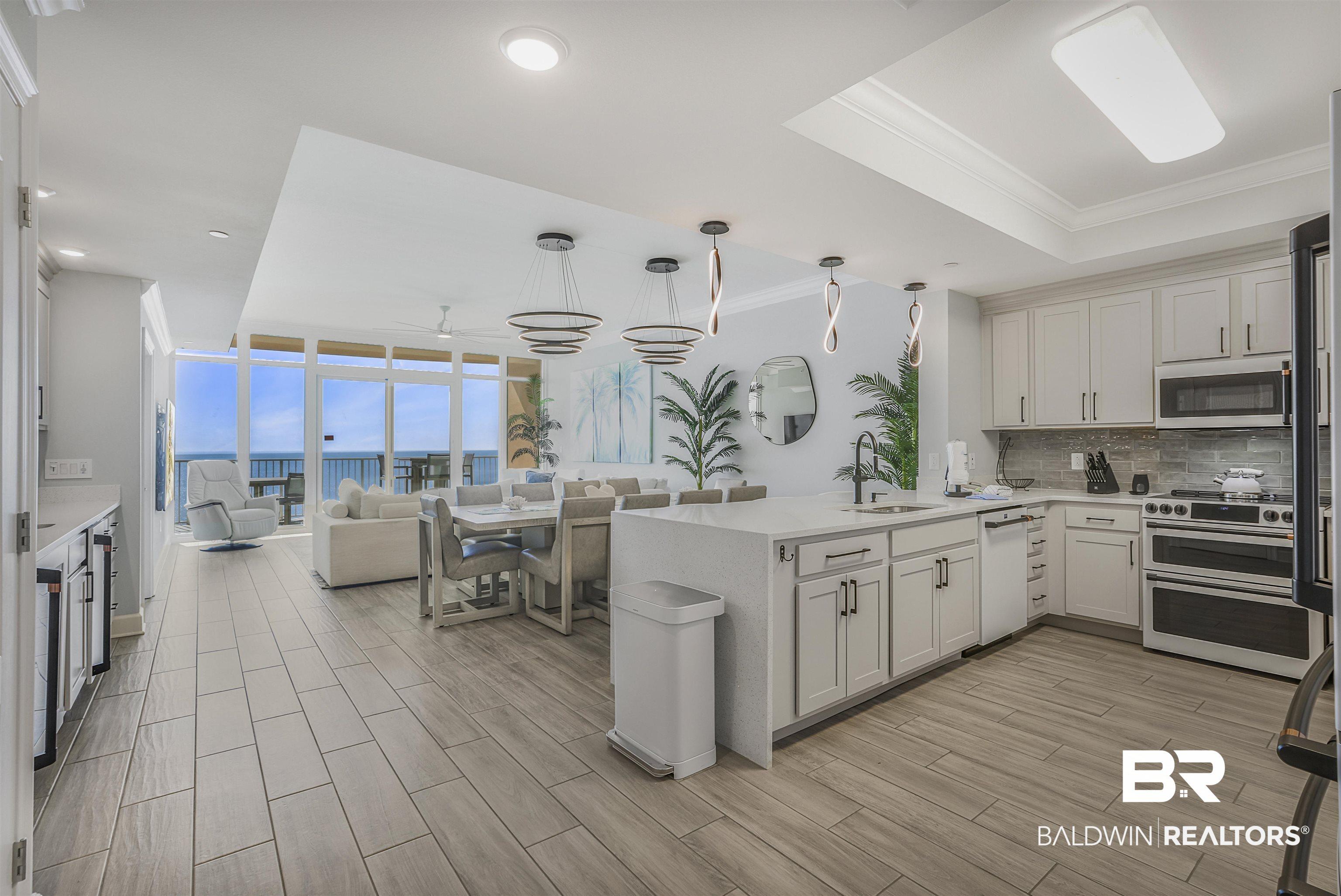 Image 3: Kitchen featuring wood tiled floors, hanging light fixtures, open floor plan, light stone countertops, and a peninsula