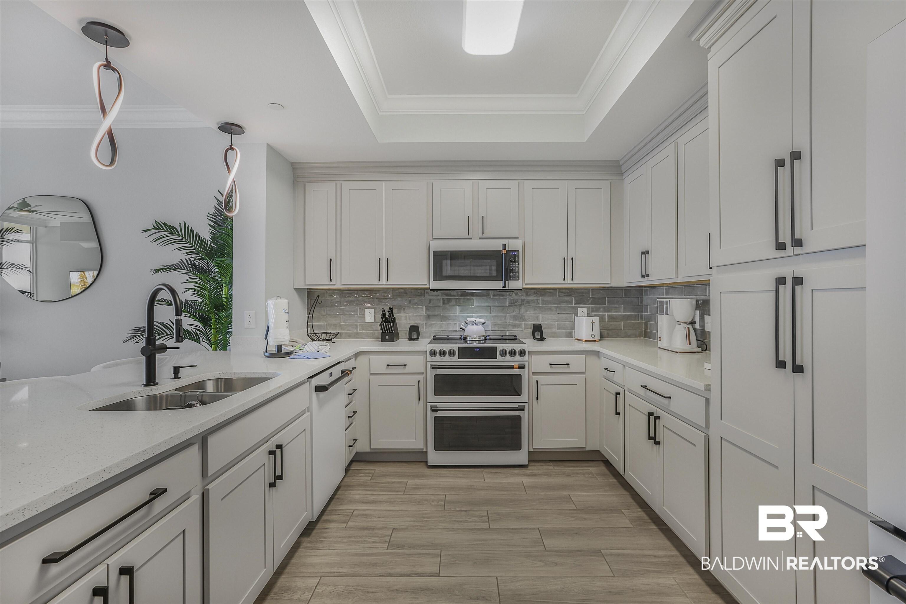 Image 4: Kitchen with stainless steel appliances, light stone countertops, crown molding, pendant lighting, and white cabinetry