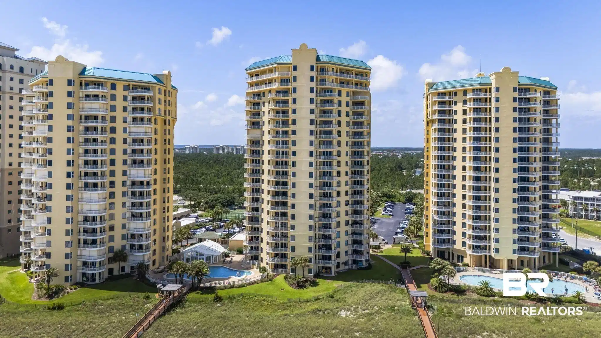 Image 1: Three high-rise buildings featuring multiple balconies, two outdoor pools, and two elevated boardwalks extending over green space