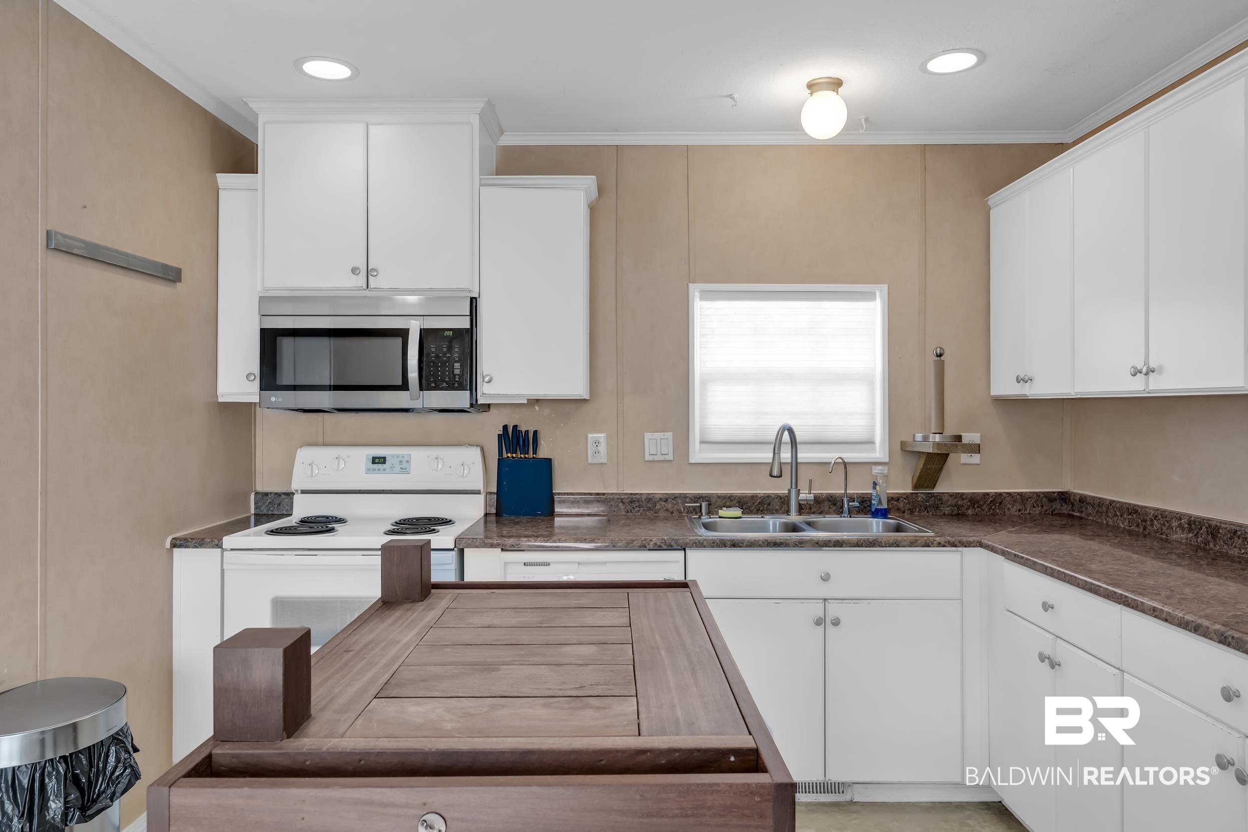 Image 4: Kitchen with white electric range, stainless steel microwave, white cabinets, dark countertops, and crown molding
