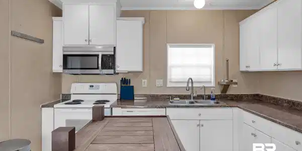 Image 4: Kitchen with white electric range, stainless steel microwave, white cabinets, dark countertops, and crown molding