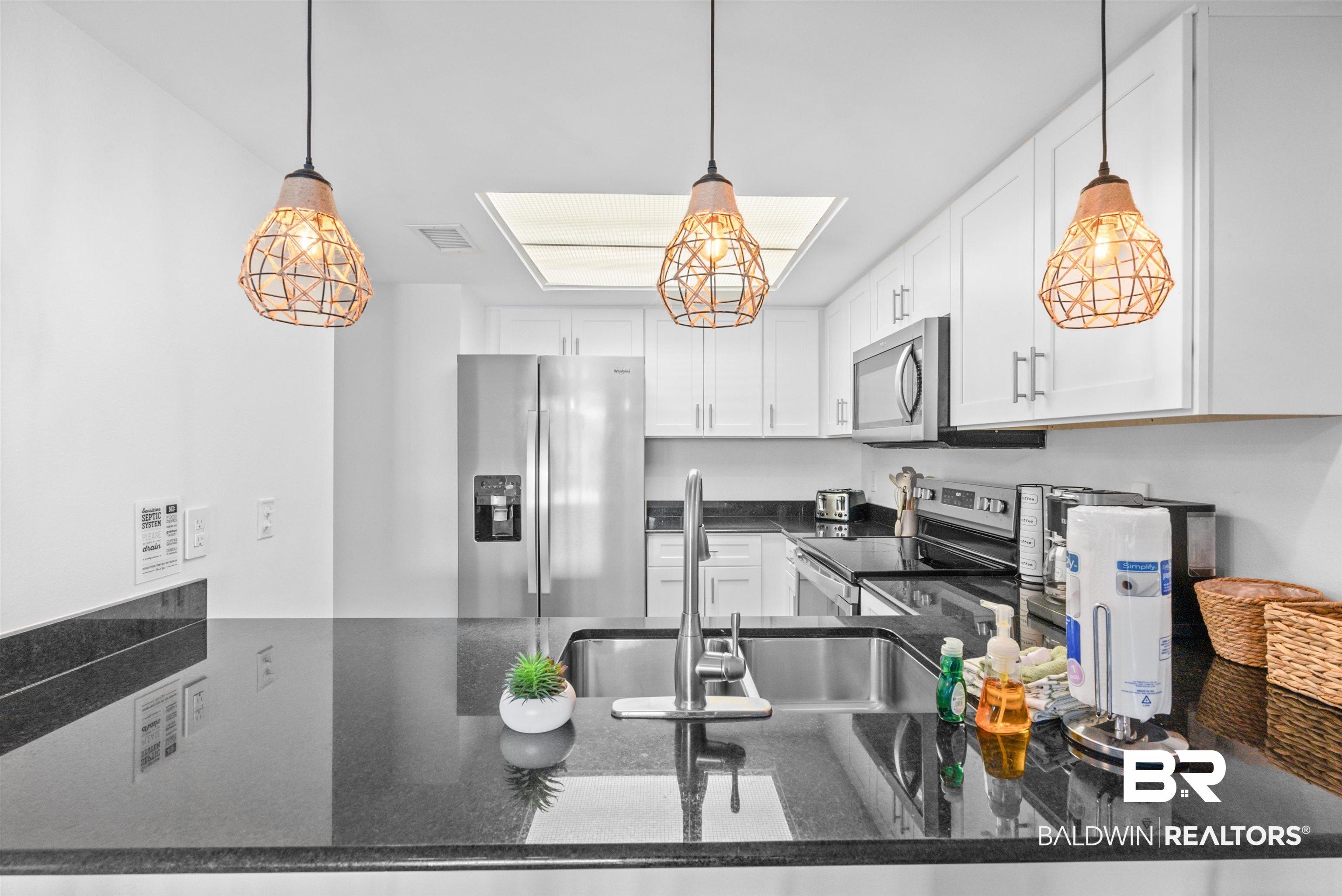 Image 4: Kitchen featuring white shaker-style cabinetry, dark countertops, stainless steel appliances, and a skylight