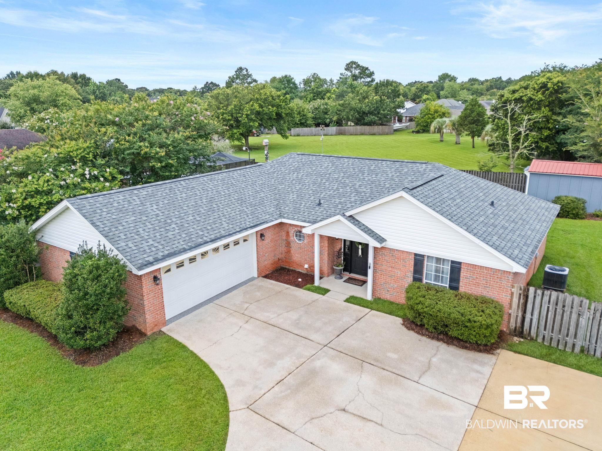 Image 4: Brick exterior residence featuring an attached garage, paved driveway, mature landscaping, and a fenced backyard with a detached shed