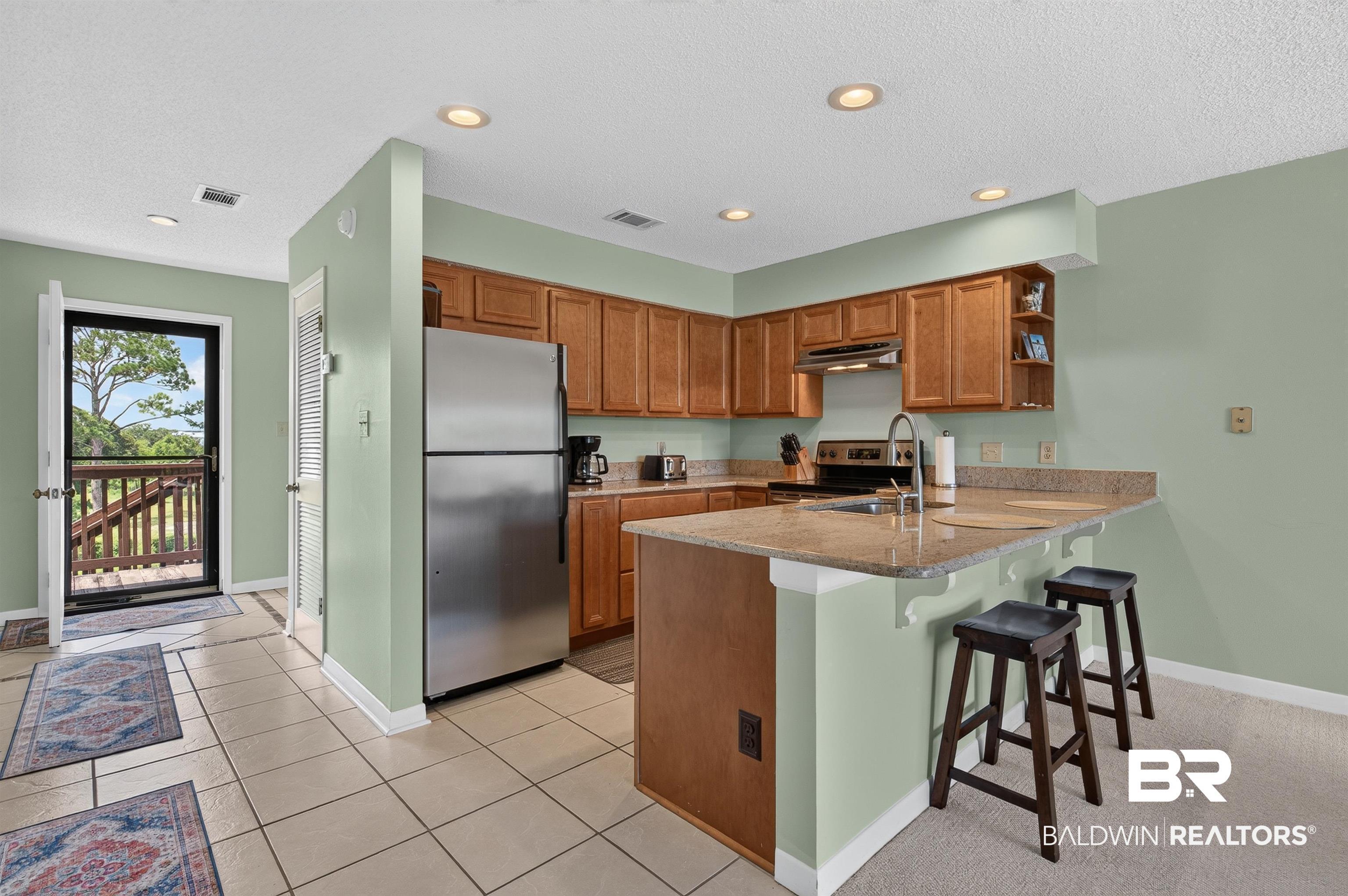 Image 4: Kitchen featuring wood-finish cabinetry, stainless steel appliances, and a peninsula with countertop seating