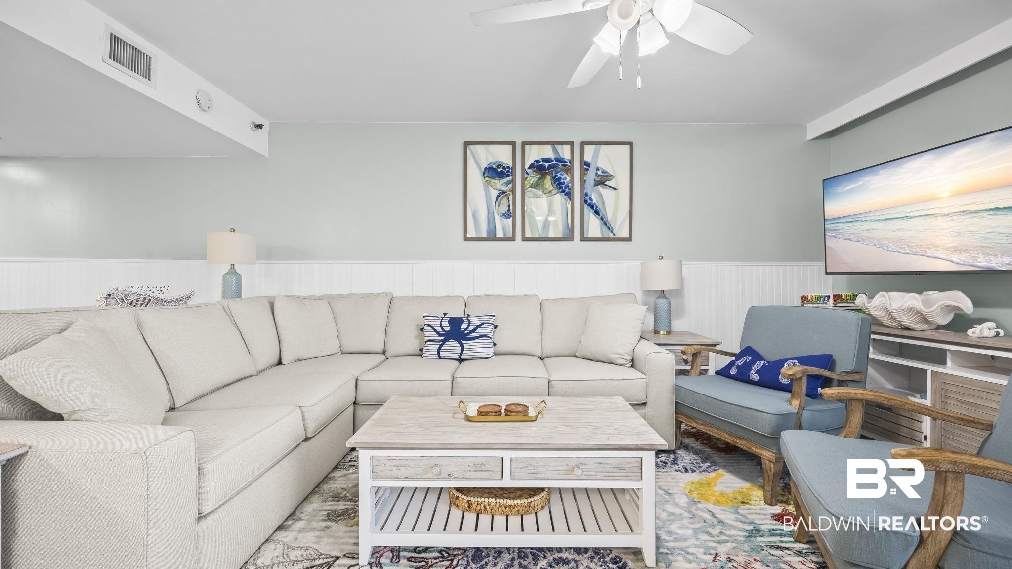 Image 3: Spacious living area featuring a neutral sectional sofa, light wood-finish coffee table, and a ceiling fan