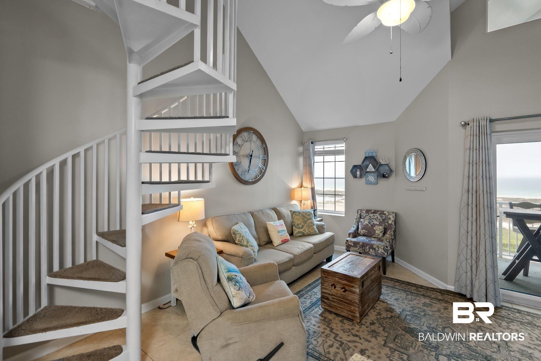 Image 4: Living area featuring a white spiral staircase with carpeted treads, vaulted ceilings, and tile flooring
