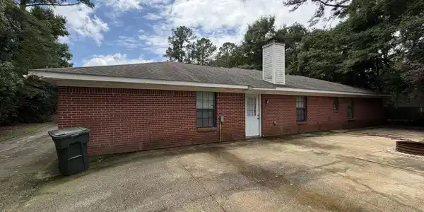 Image 2: Brick exterior featuring multiple windows and a white exterior door