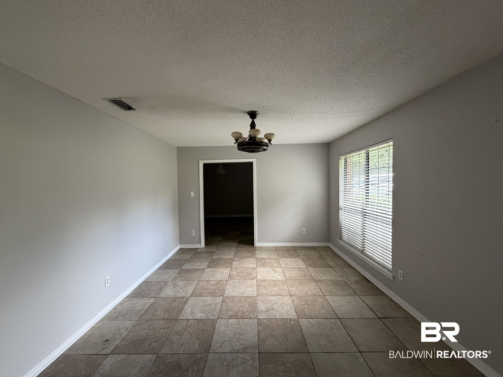 Image 4: Spacious room with large-format tile flooring, neutral wall paint, and a multi-light ceiling fixture
