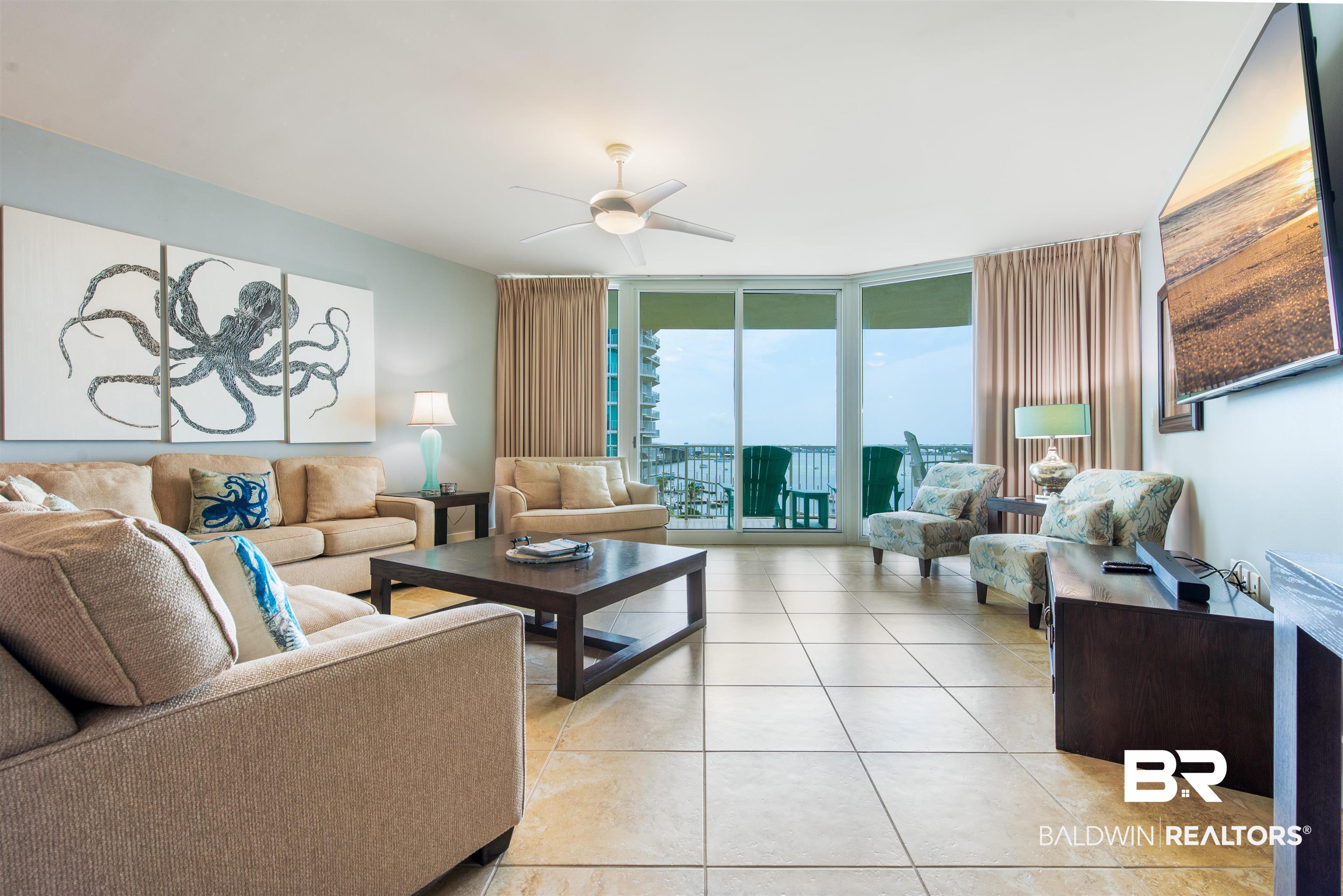 Image 2: Spacious living area featuring neutral-toned tile flooring, light blue wall paint, a ceiling fan with integrated lighting, and expansive glass sliding doors opening to an outdoor area