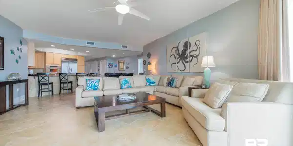 Image 3: Open-concept living space featuring light-toned tile flooring, a recessed ceiling with a white ceiling fan, and a kitchen area with light wood cabinetry and stainless steel appliances