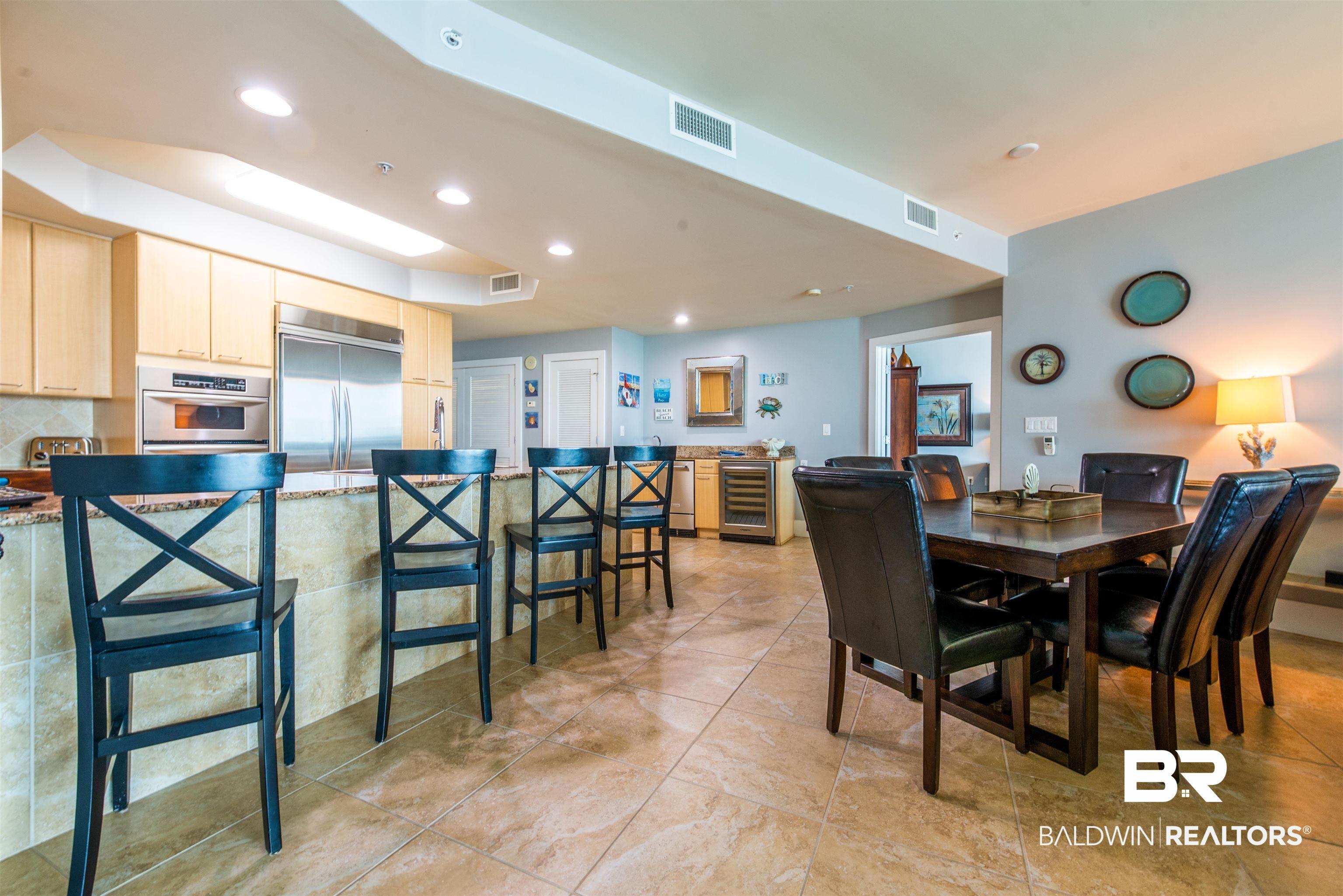 Image 4: Open concept living area featuring light-toned cabinetry, stainless steel appliances, a breakfast bar with stone-finish countertop, and tiled flooring