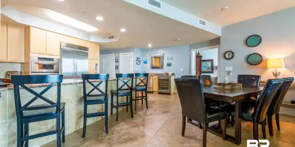Image 4: Open concept living area featuring light-toned cabinetry, stainless steel appliances, a breakfast bar with stone-finish countertop, and tiled flooring