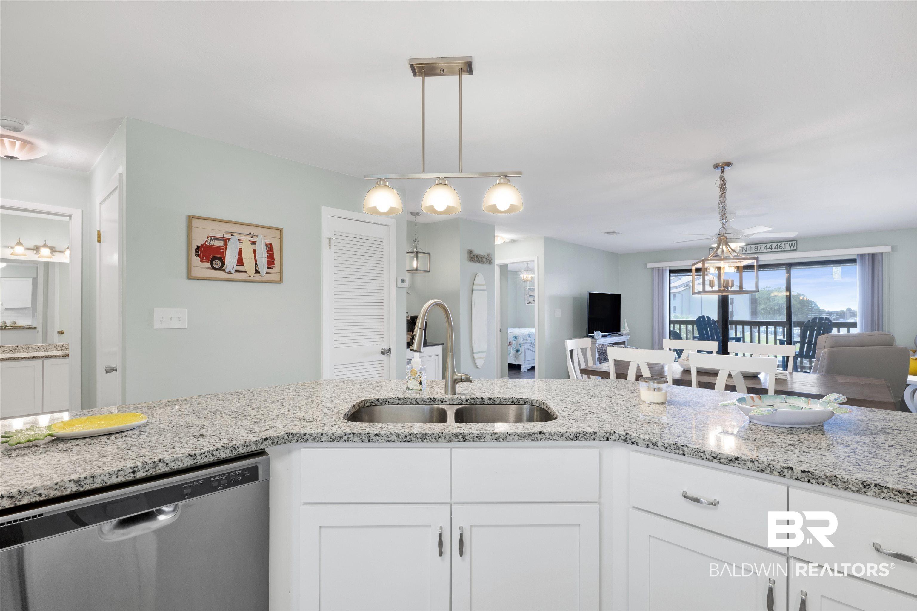 Image 4: Kitchen featuring granite-style countertops, white cabinetry, a stainless steel sink, and a modern pendant light fixture