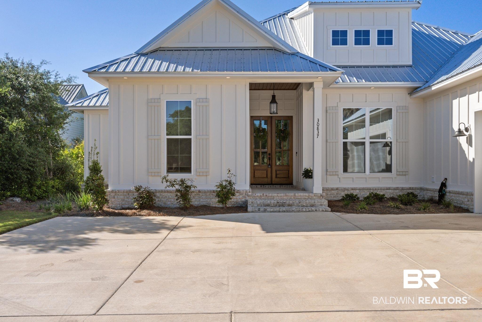 Image 4: Contemporary coastal exterior featuring vertical board and batten siding, a metal roof, and a stone-clad foundation