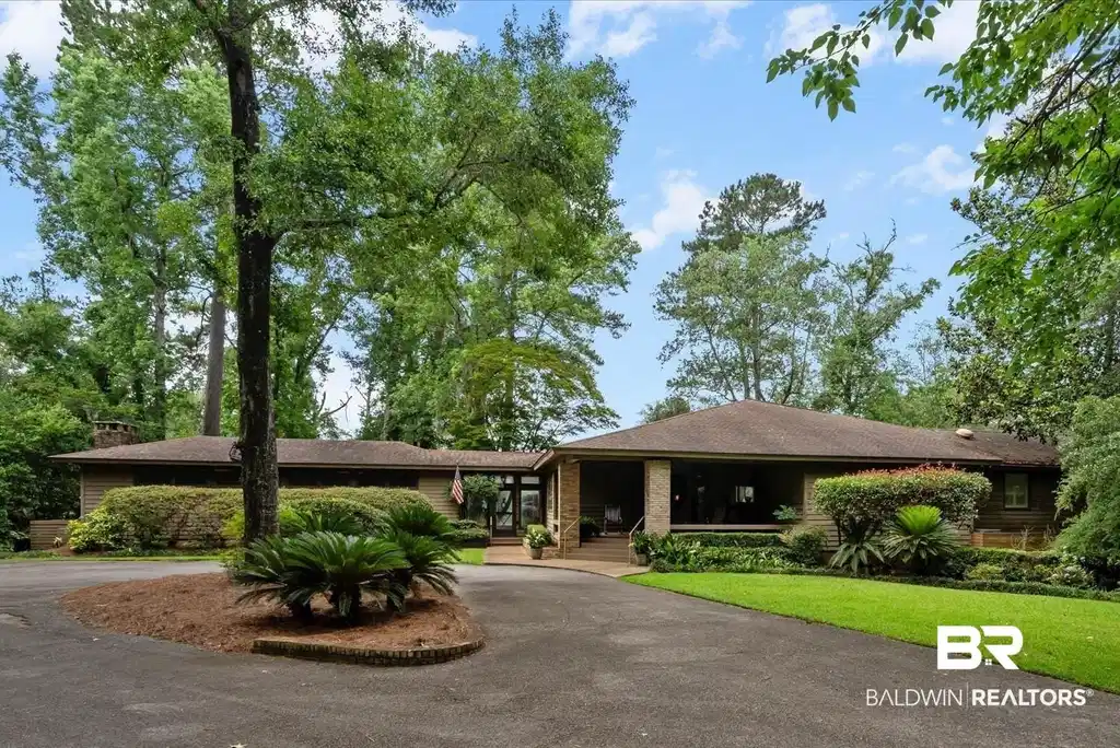 Image 1: Ranch-style residence featuring a paved circular driveway, mature trees, manicured landscaping, a covered front porch, and an attached garage with a glass door