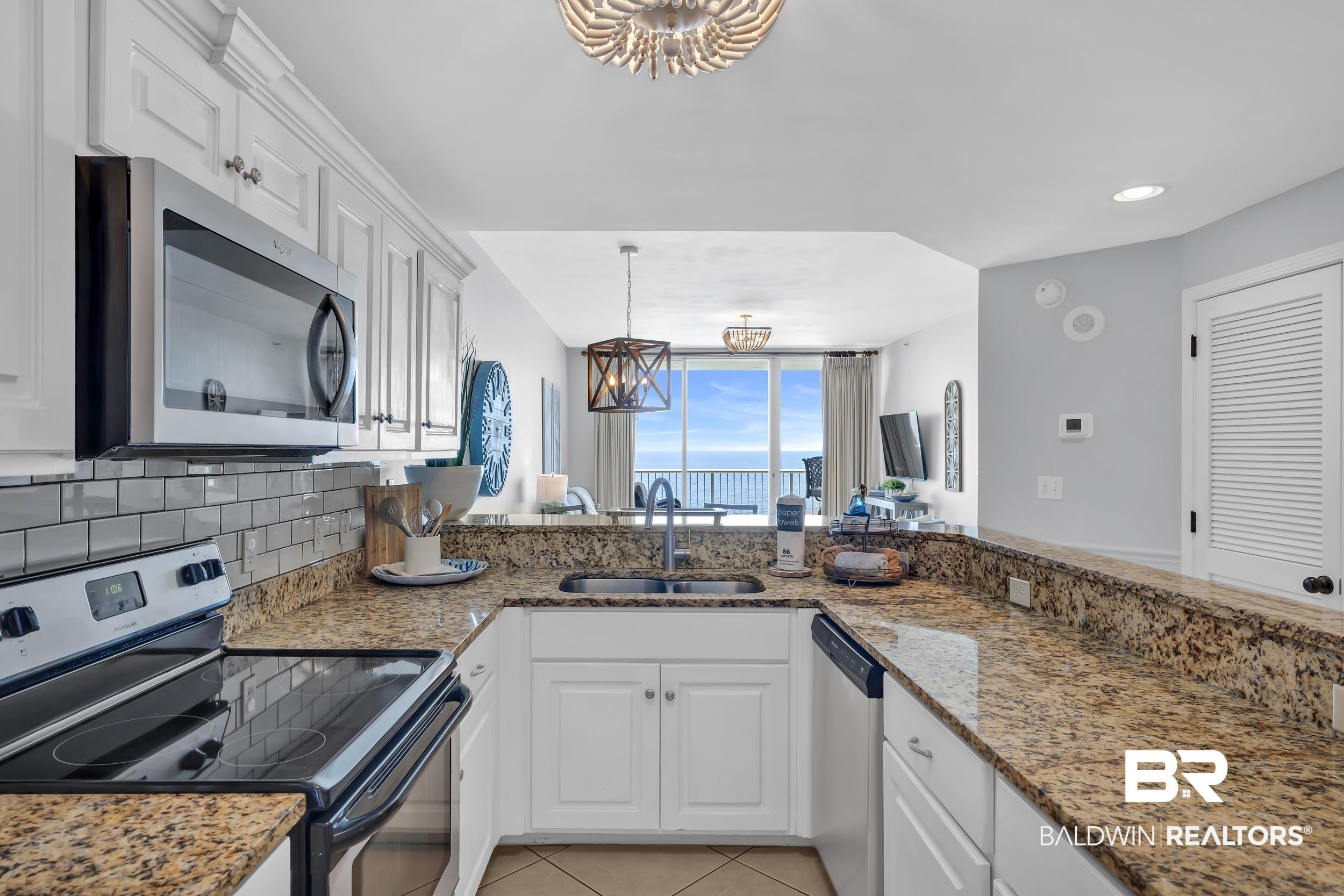 Image 3: U-shaped kitchen featuring white cabinetry, granite countertops, stainless steel appliances, and a subway tile backsplash