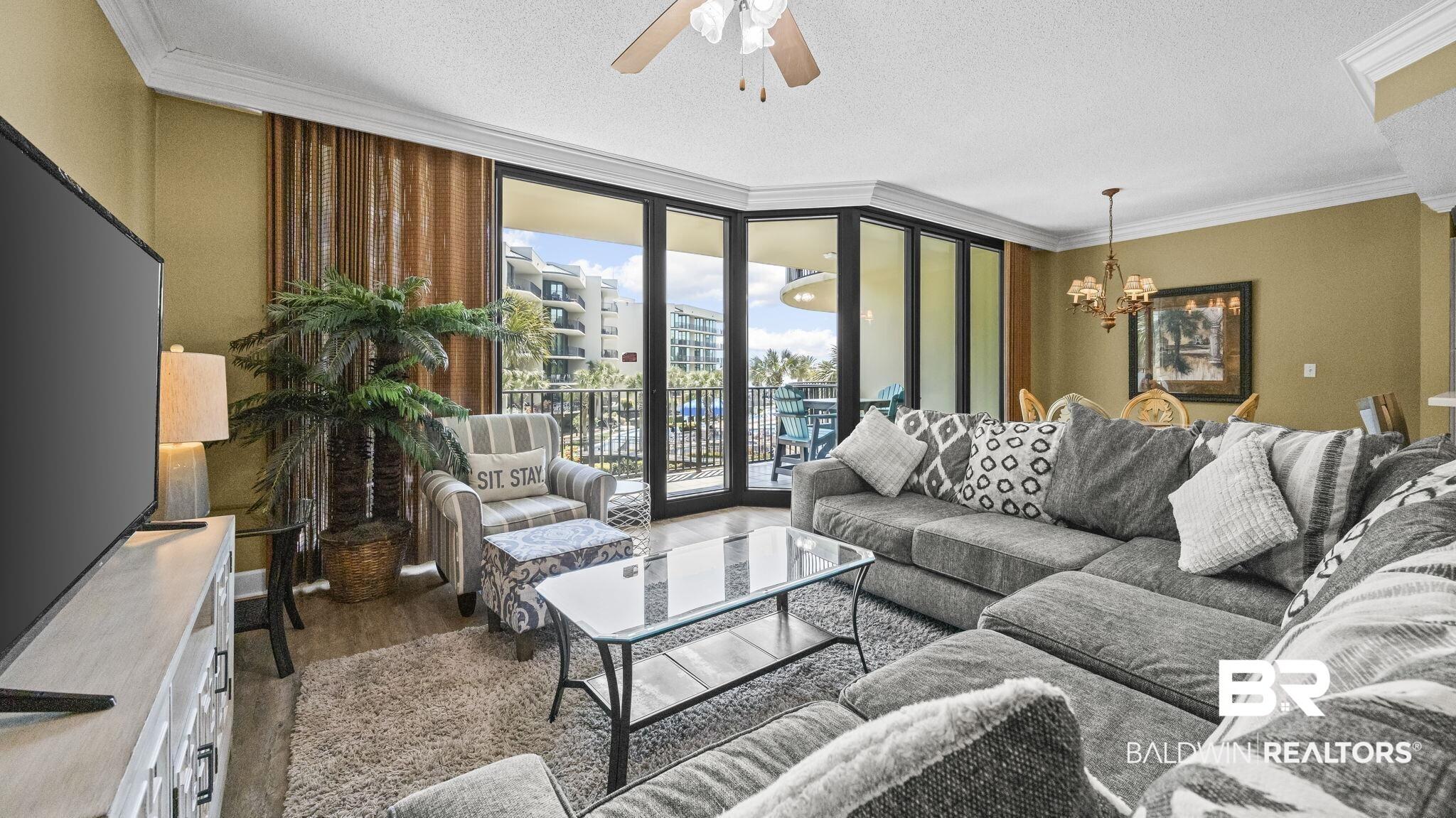Image 2: Living room featuring expansive windows, ceiling fan, ornamental molding, hanging lights, and dark wood-style flooring