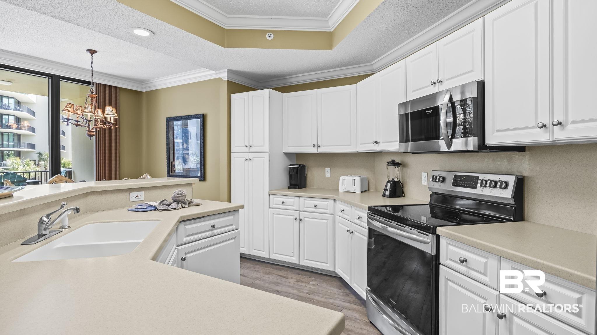 Image 4: Kitchen featuring stainless steel appliances, white cabinetry, light countertops, a chandelier, and a textured ceiling