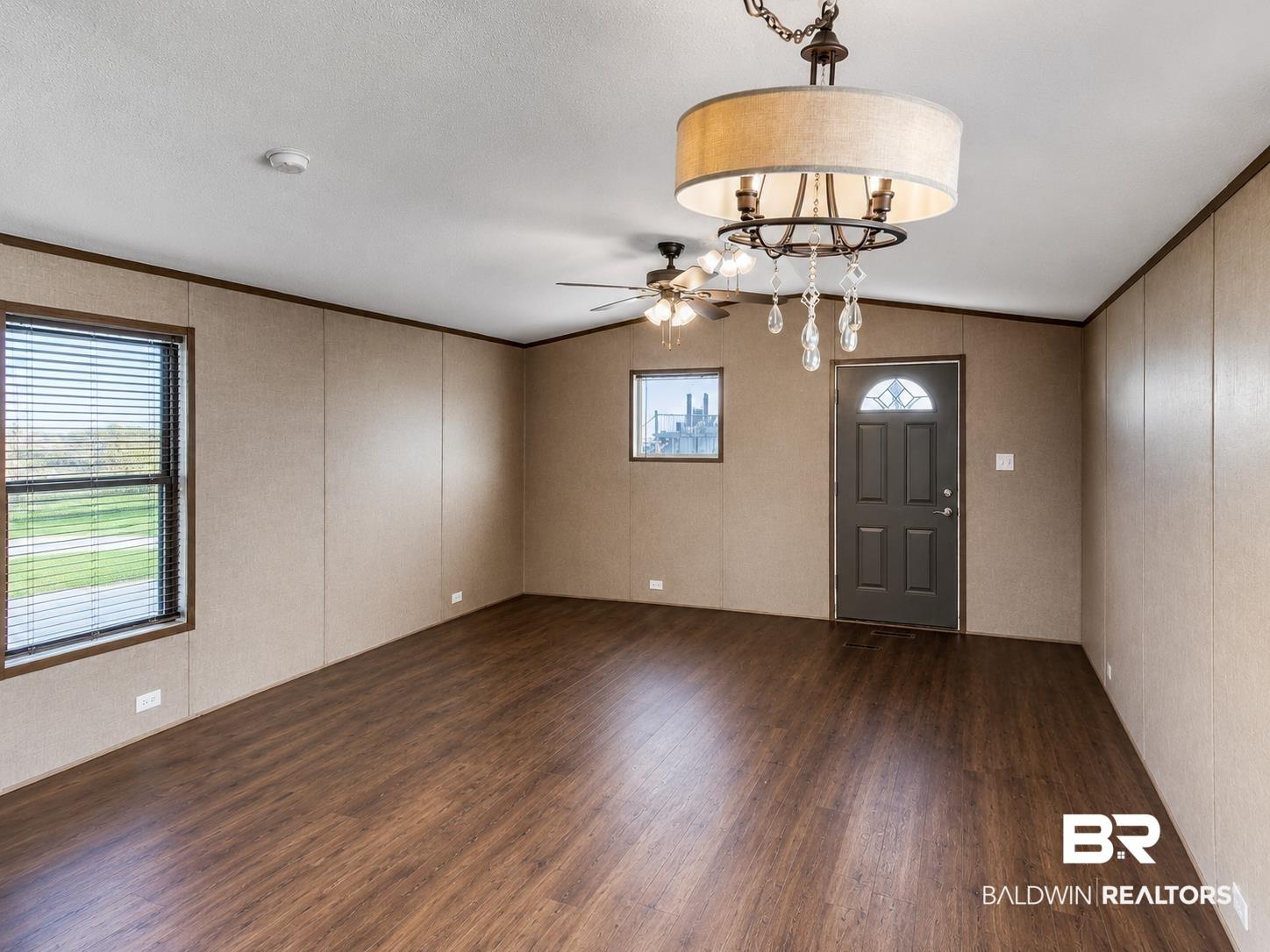 Image 2: Spacious interior featuring wood-finish flooring, a paneled entry door with decorative glass, and a drum-shade chandelier with crystal accents