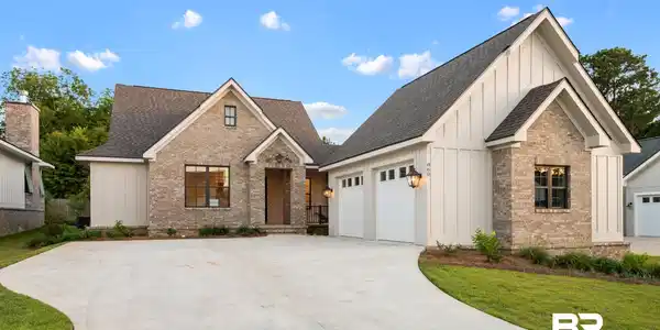 Image 3: Contemporary home featuring a light brick facade, white vertical siding, dark shingle roofing, and a concrete driveway