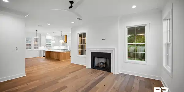 Image 4: Open-concept living area with wood-finish flooring, a contemporary fireplace with a white surround, recessed lighting, and a modern ceiling fan