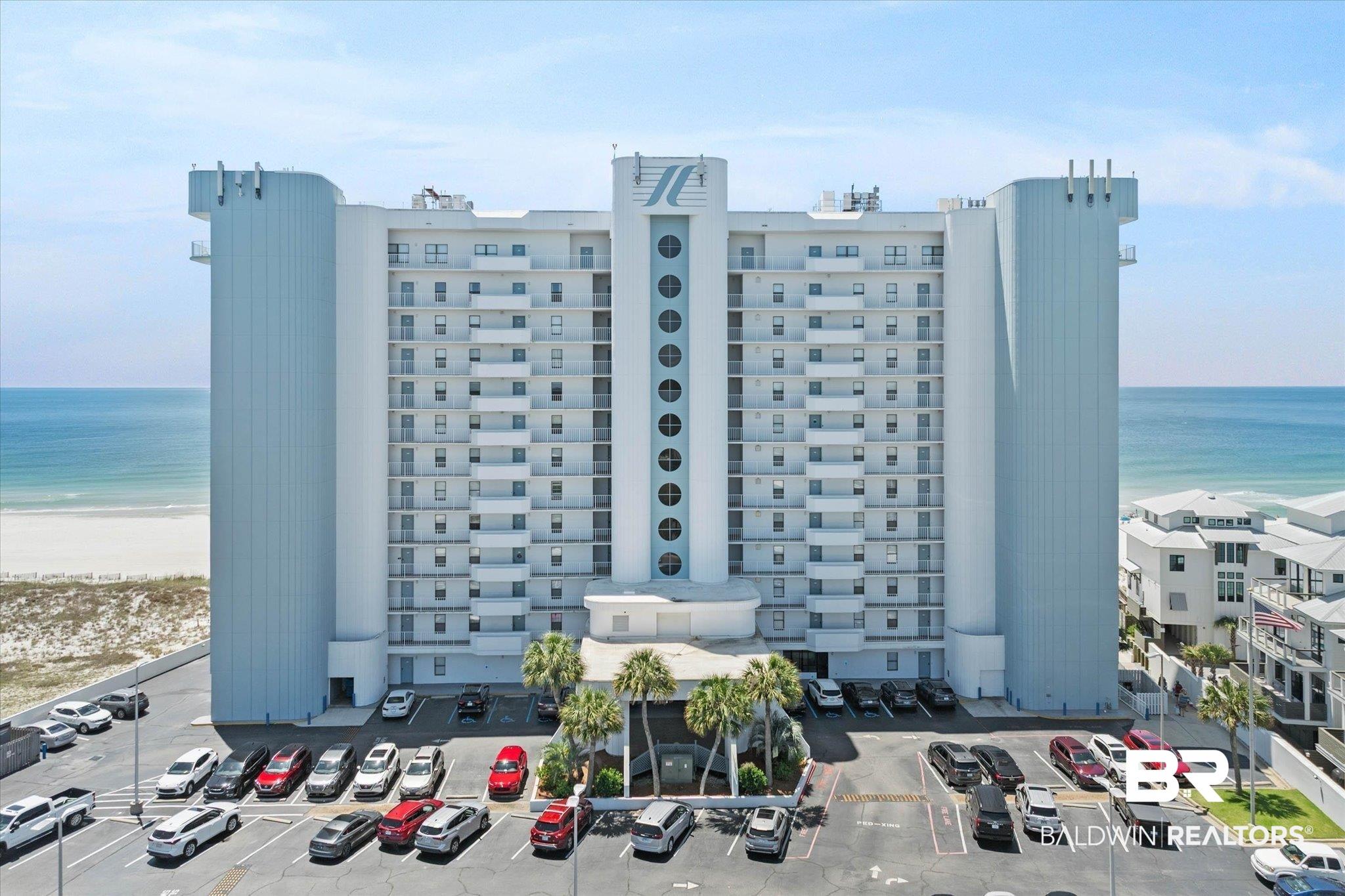 Image 1: Multi-story building featuring numerous balconies, a beachfront location, and a spacious parking lot
