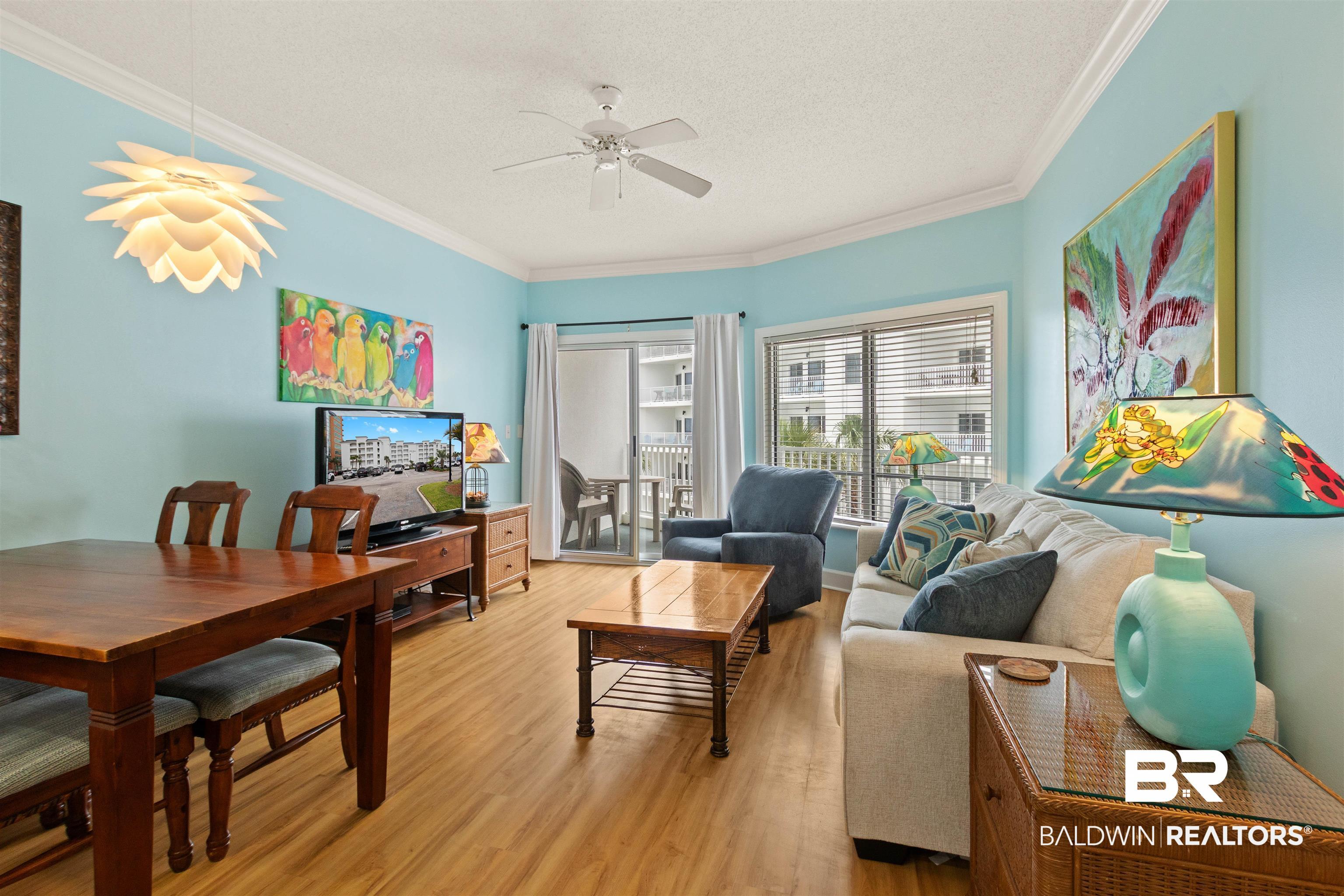 Image 3: Open-concept living area with wood-finish flooring, a contemporary pendant light fixture, and crown molding