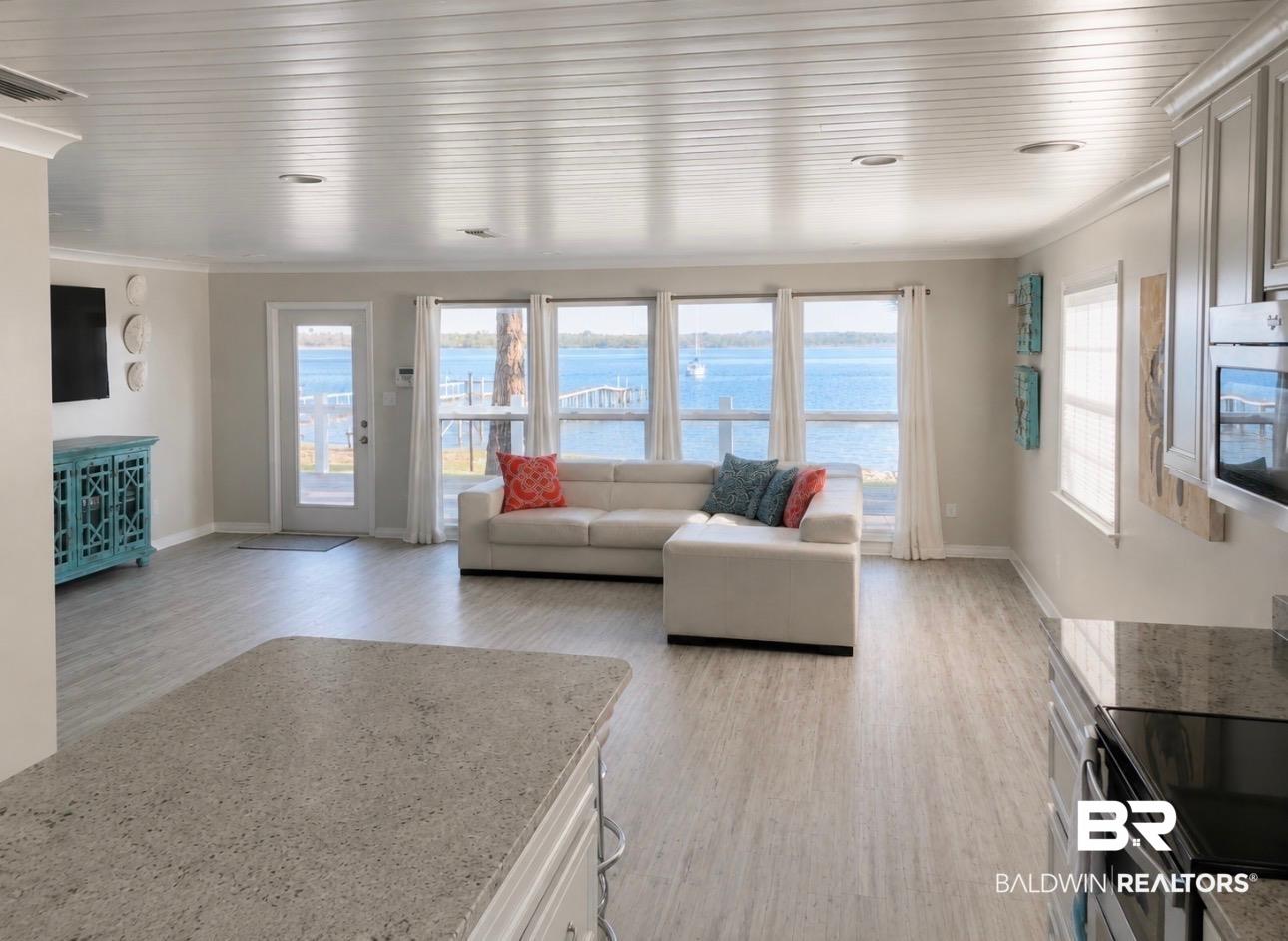 Image 2: Open-concept living area with water frontage, wide plank wood-finish flooring, recessed lighting, and a kitchen island with a stone countertop