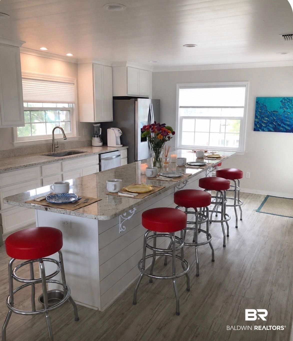 Image 3: Spacious kitchen featuring an extended island with granite-style countertops, white shaker cabinetry, stainless steel appliances, and wood-finish flooring
