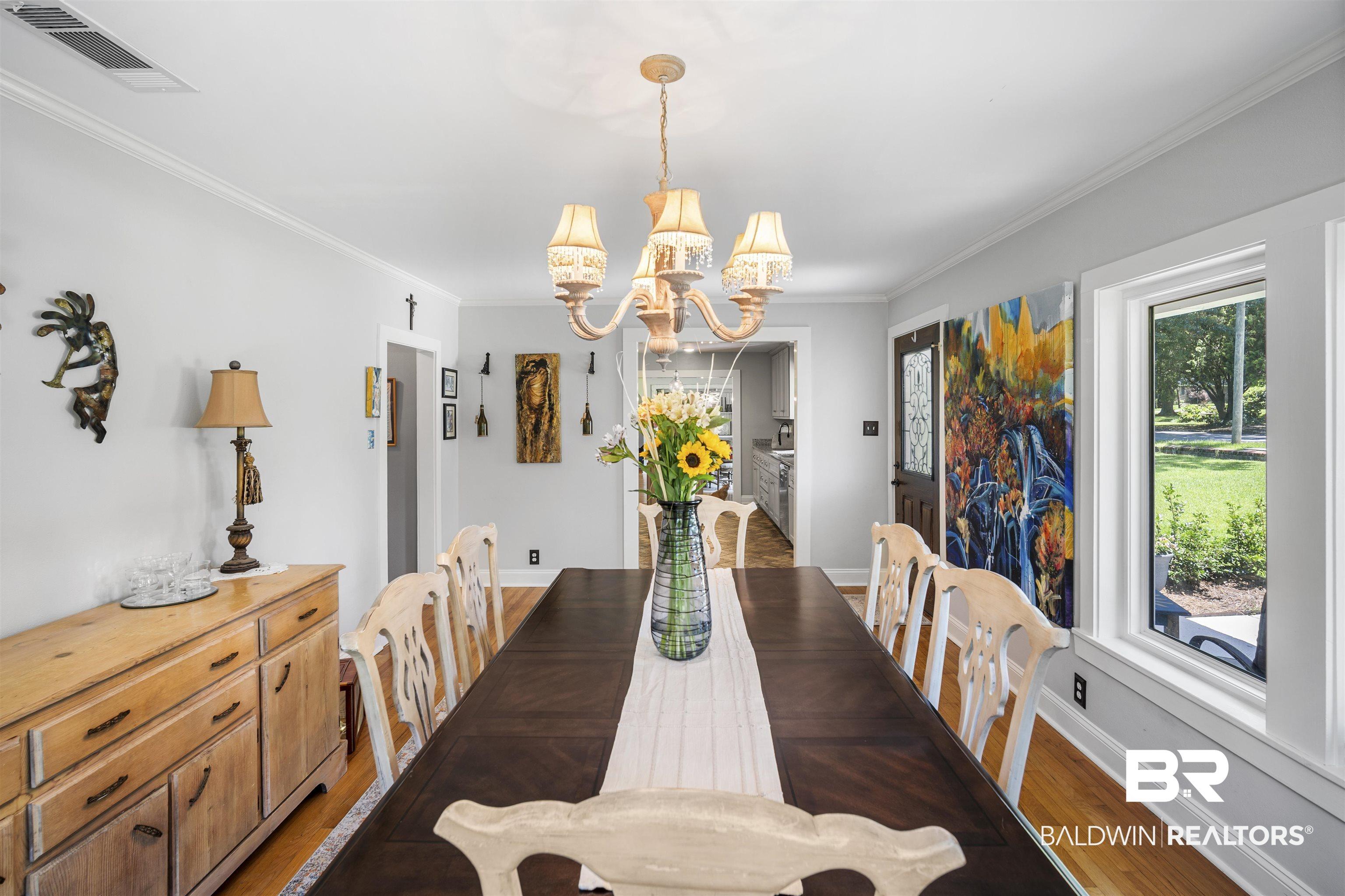 Image 3: Spacious dining area featuring wood-finish flooring, a traditional chandelier, crown molding, and ample natural light from a large window