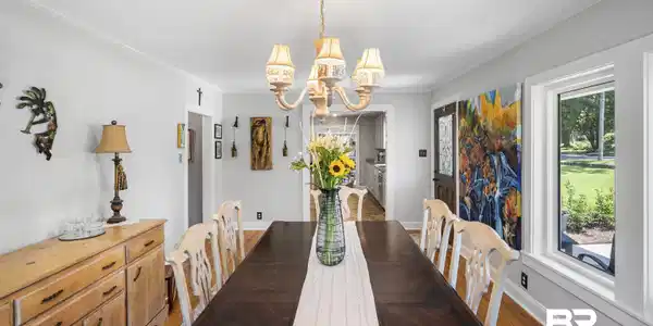 Image 3: Spacious dining area featuring wood-finish flooring, a traditional chandelier, crown molding, and ample natural light from a large window