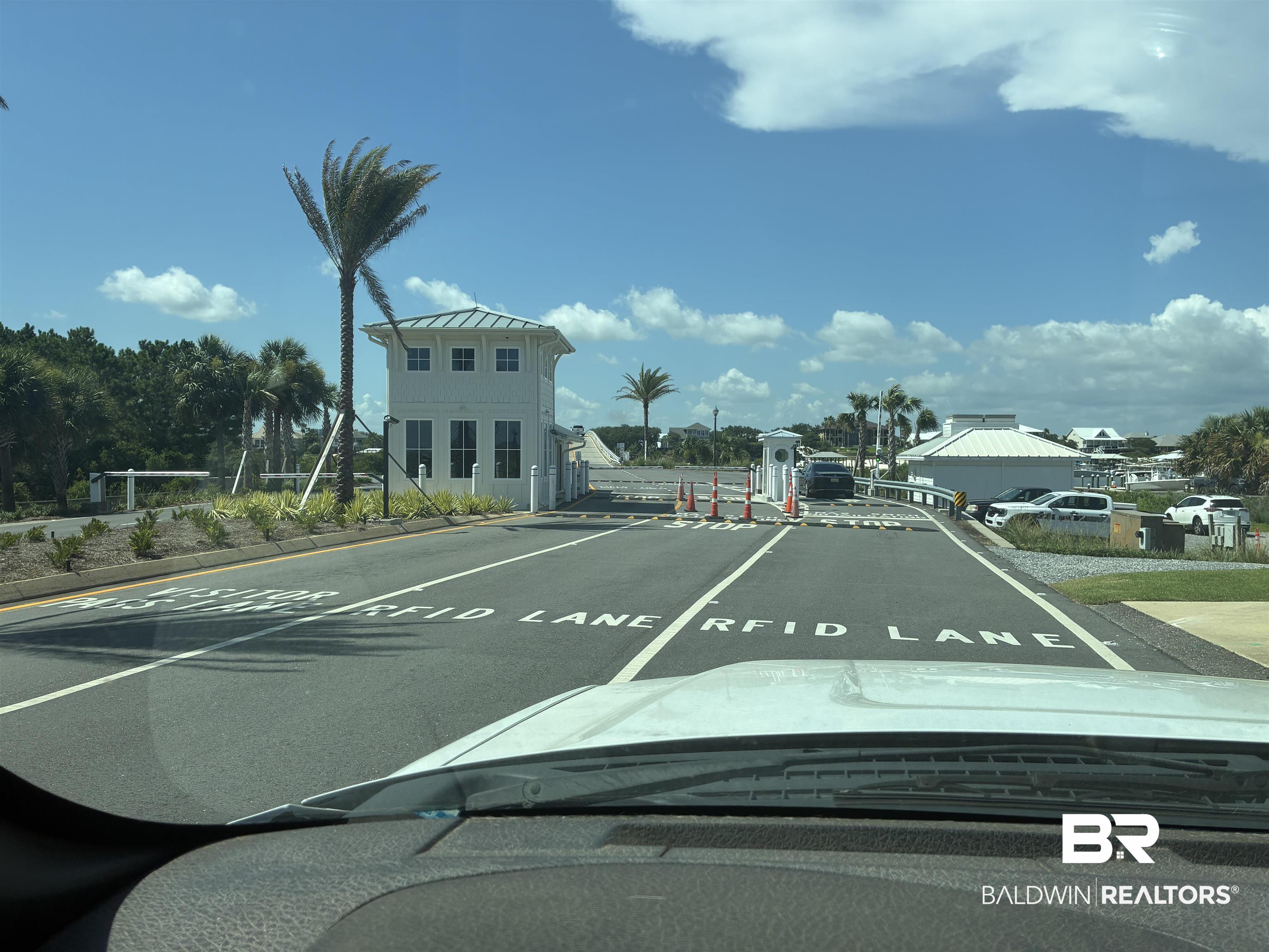 Image 2: Community entrance featuring a multi-lane access point, white architectural gatehouse, and established palm trees