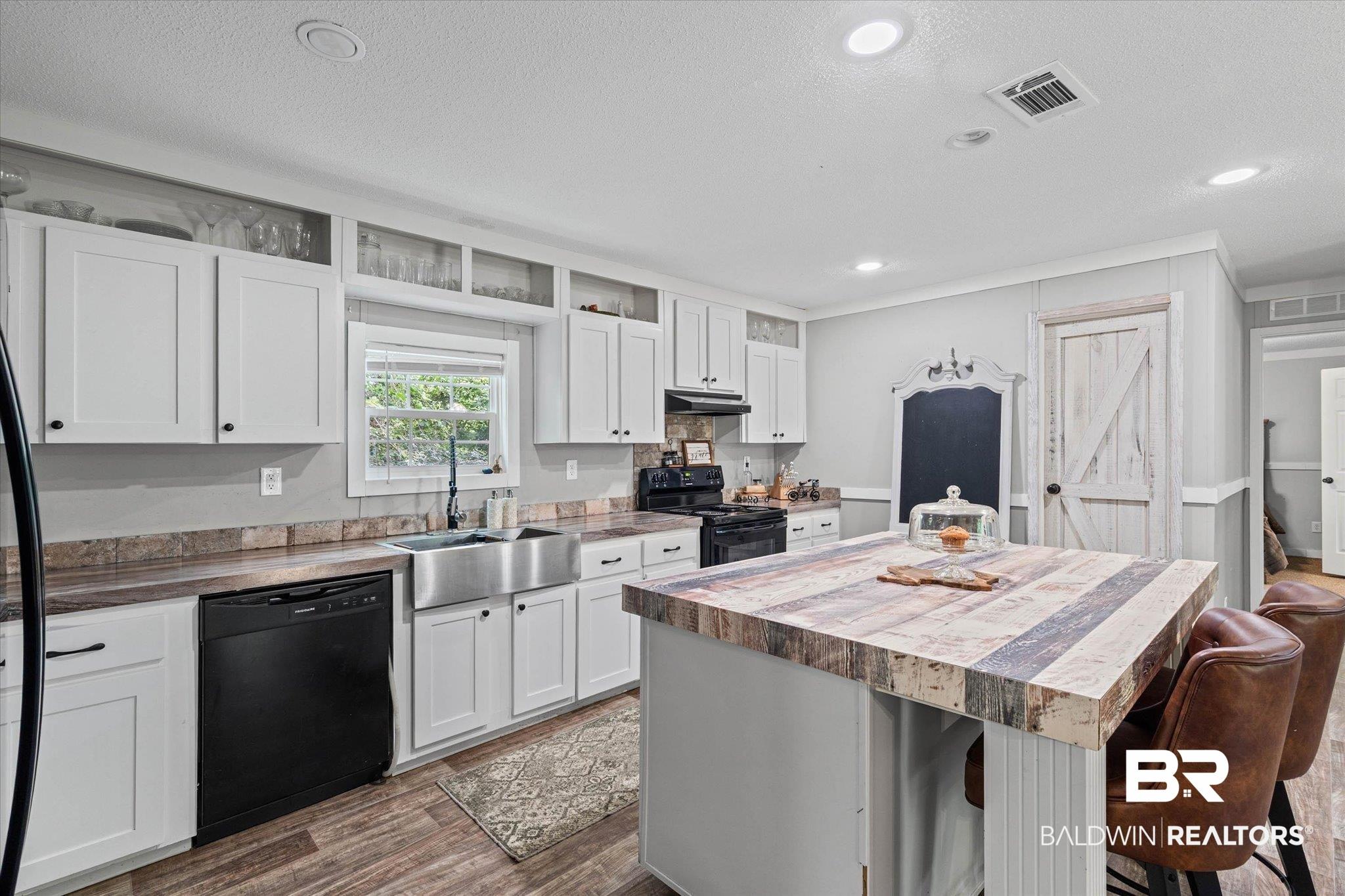 Image 2: Kitchen featuring a large central island with wood-finish countertop, white cabinetry with black hardware, stainless steel farmhouse sink, and wood-finish flooring