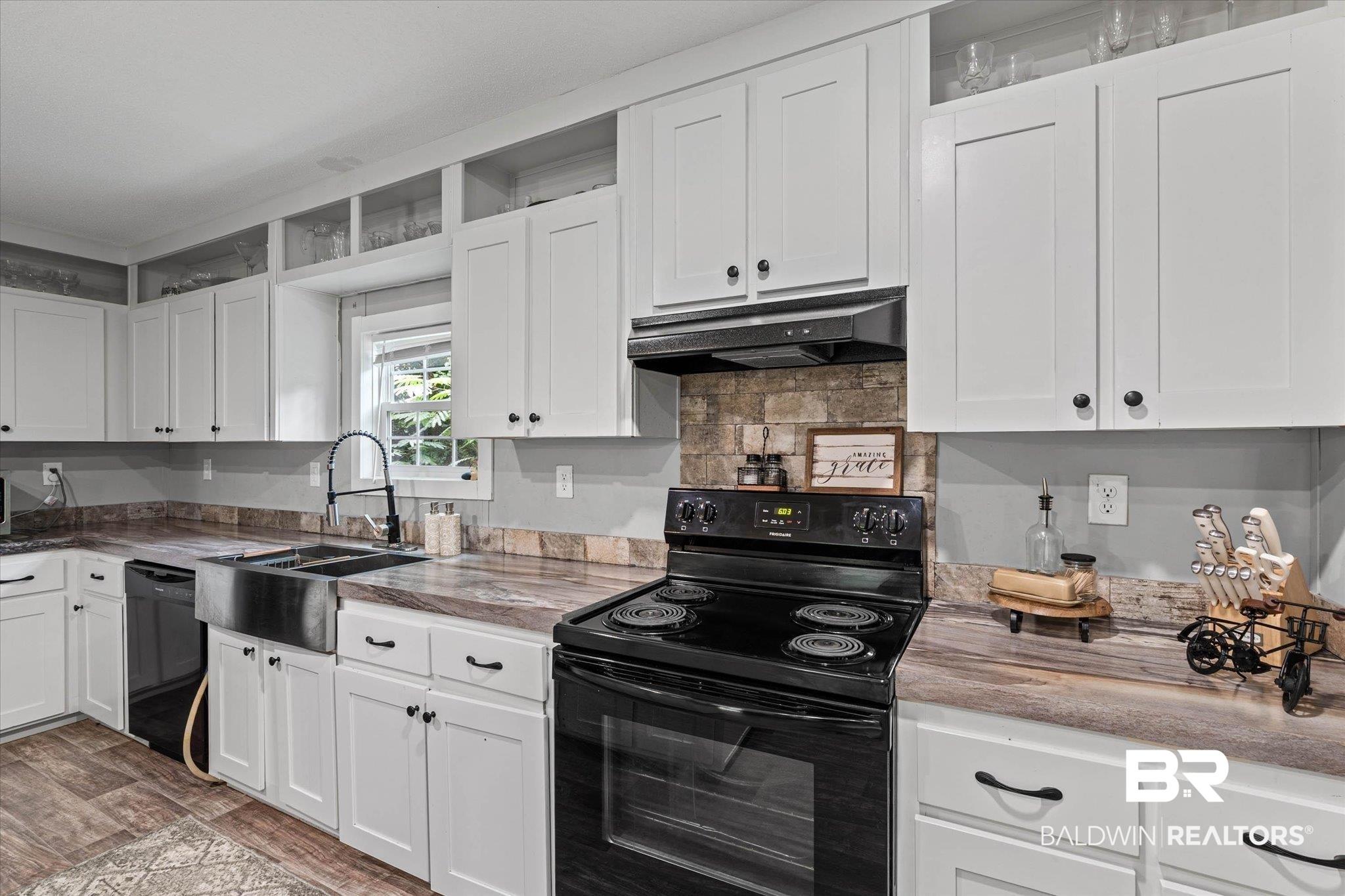 Image 4: Contemporary kitchen featuring white cabinetry, a stainless steel farmhouse sink, wood-finish flooring, a black electric range, and laminate countertops
